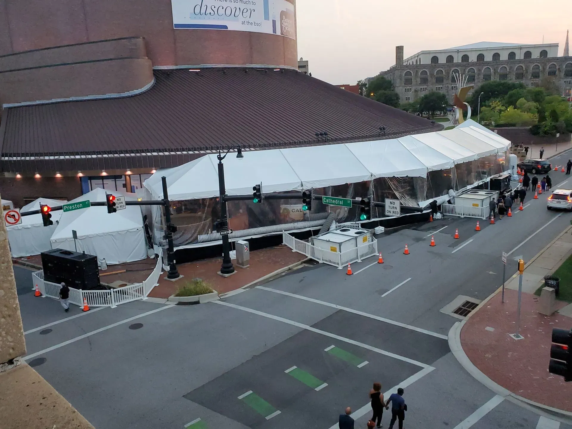 A large white tent structure erected on a city street corner adjacent to a brick building, with nearby traffic signals.