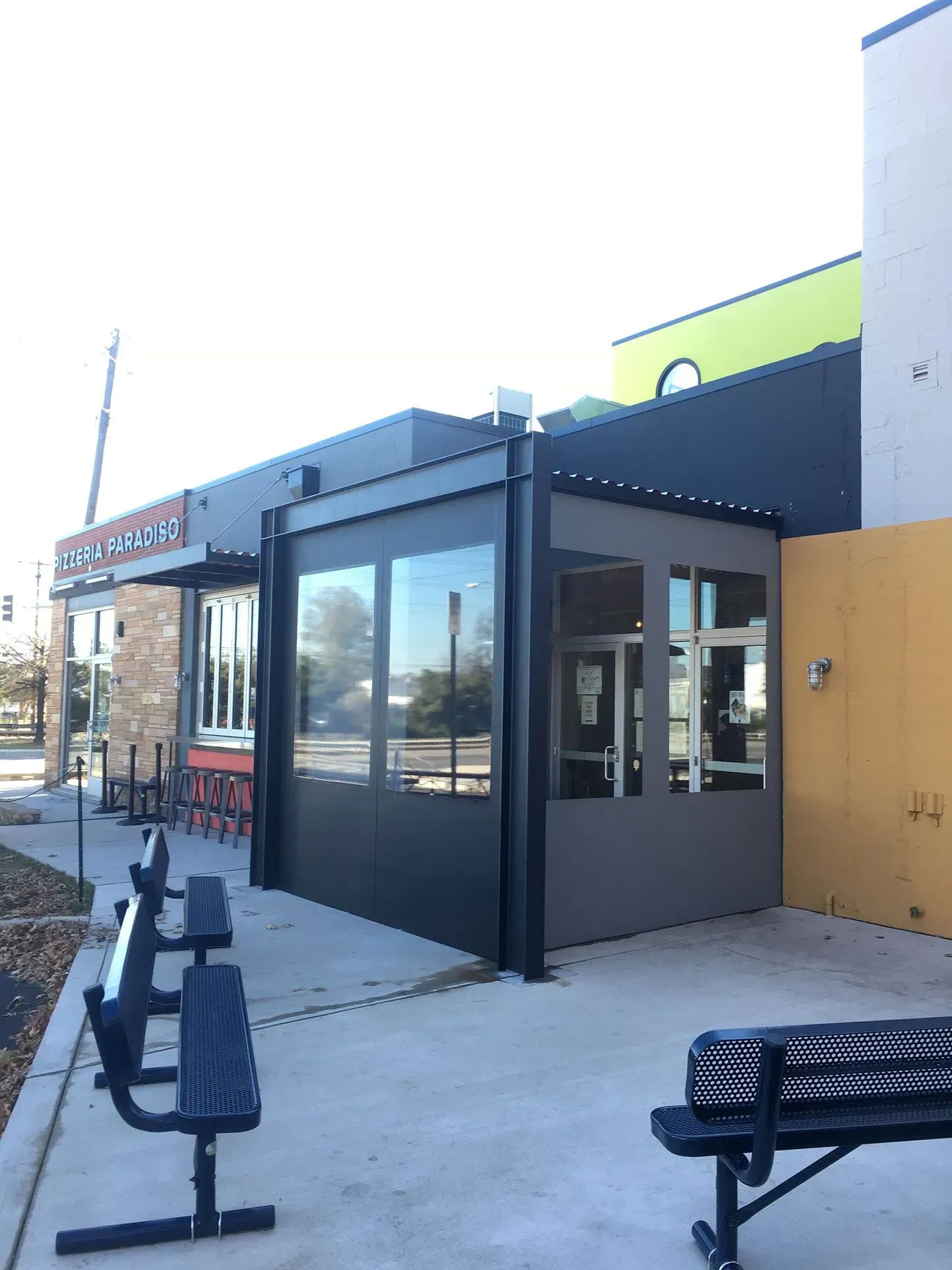 Exterior view of a building with a dark framed, glass-enclosed patio addition and two outdoor benches.