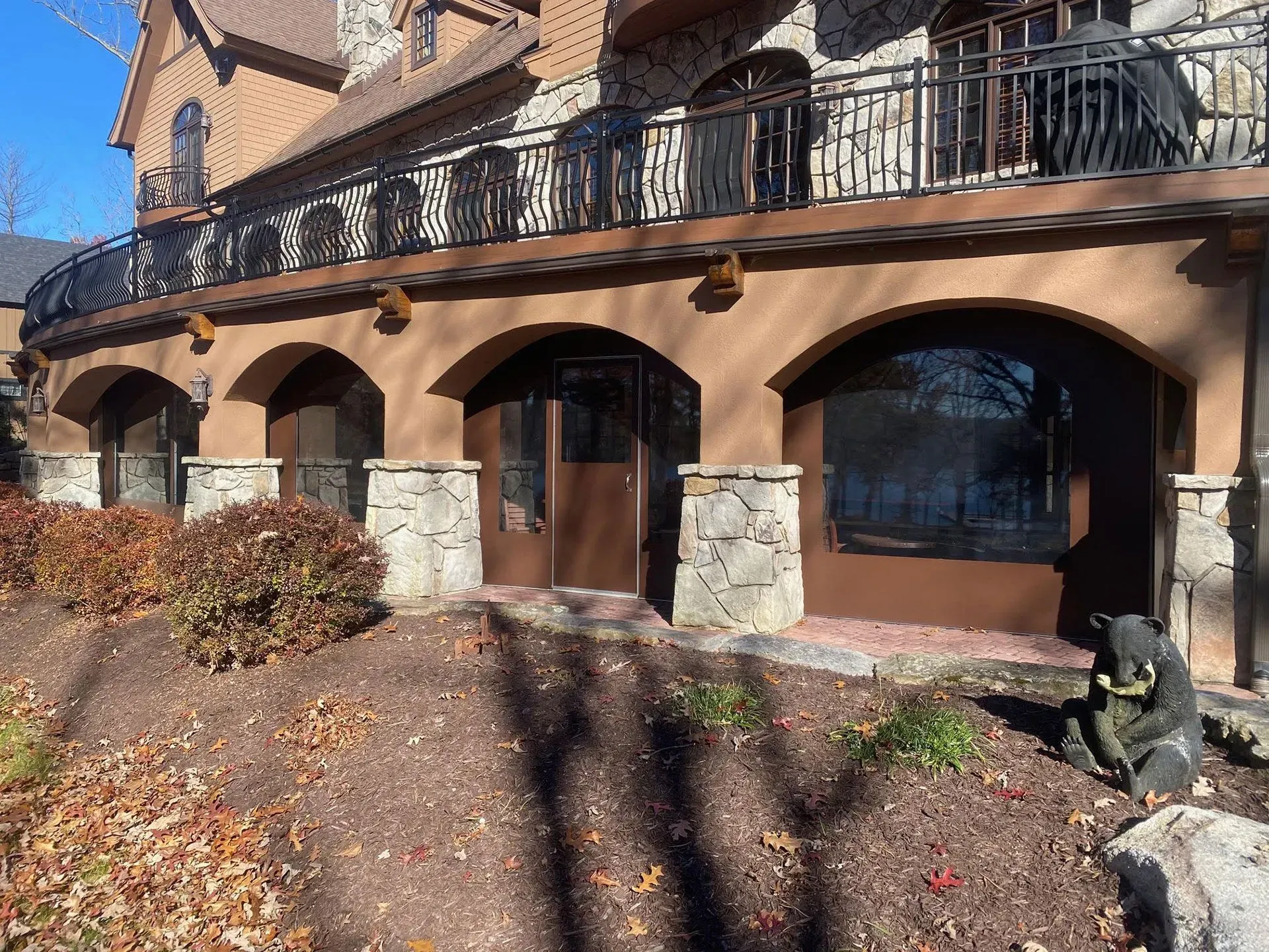 A stone-accented home exterior with a covered, arched patio area, a black metal railing, and a bear statue in the garden.