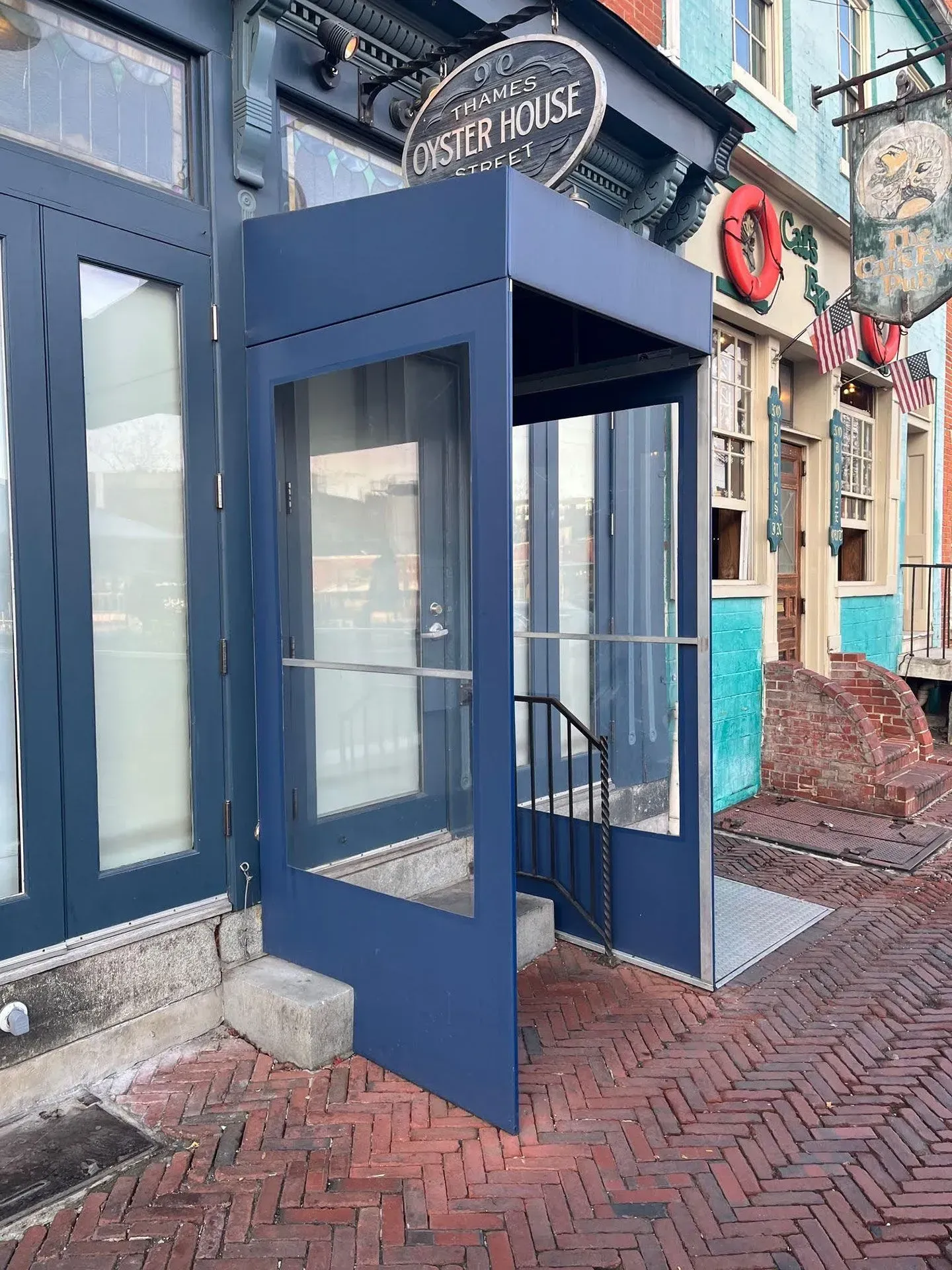 A blue, enclosed stairway entrance to the Oyster House, set on a brick sidewalk next to a historic building.