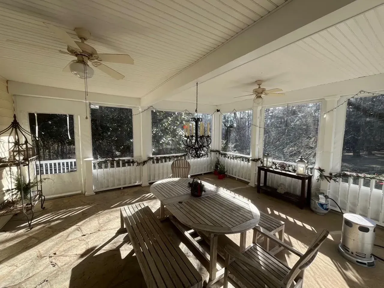 A sunlit, screened-in porch featuring a wooden dining table, benches, chairs, and ceiling fans.