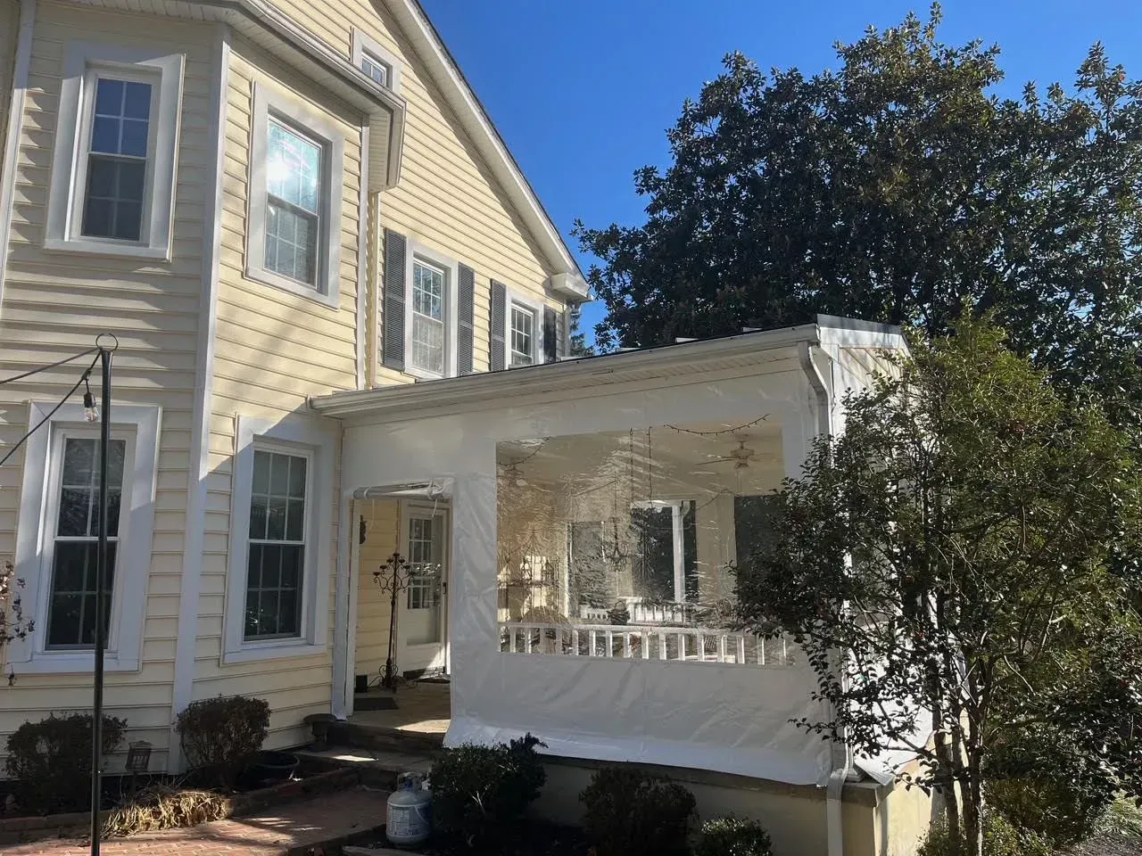 A yellow two-story house with a white-enclosed patio structure featuring large clear vinyl windows.