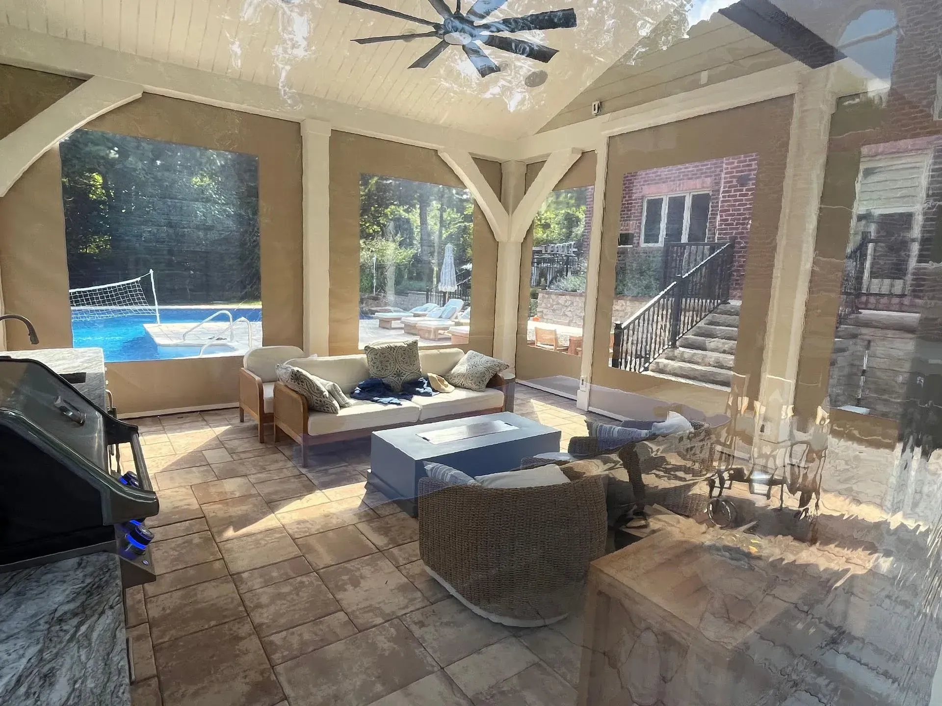 A covered outdoor patio featuring lounge seating, a coffee table, and a pool in the background on a sunny day.