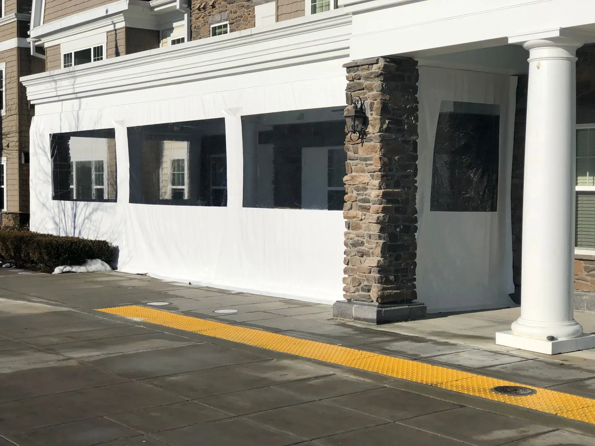 White storefront with stone columns and black awnings beside a sidewalk and curb ramp