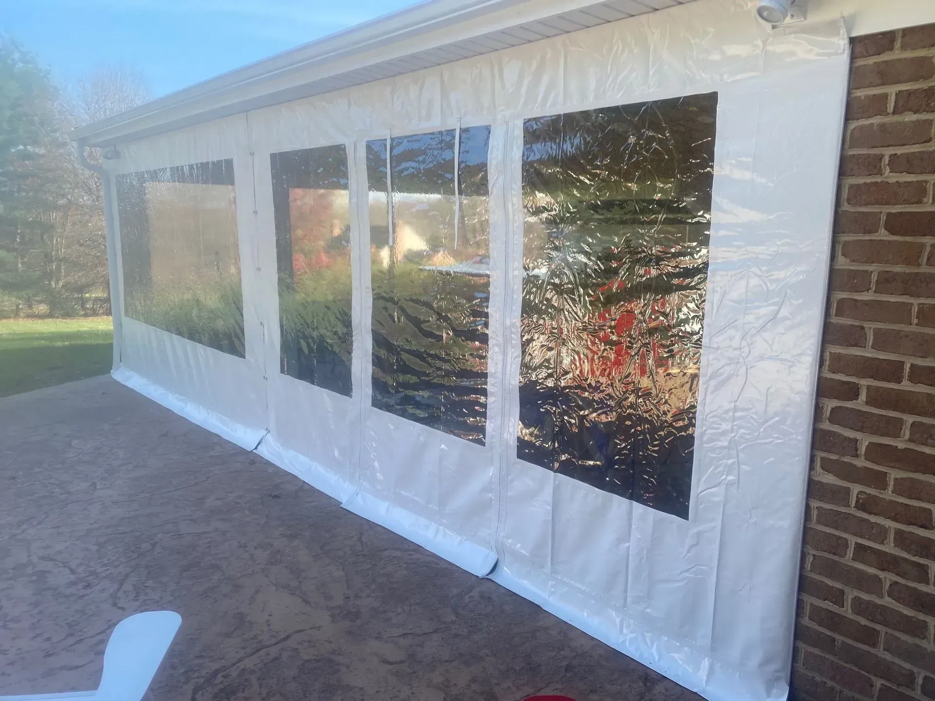 White enclosed patio tent with clear window panels attached to a house exterior.