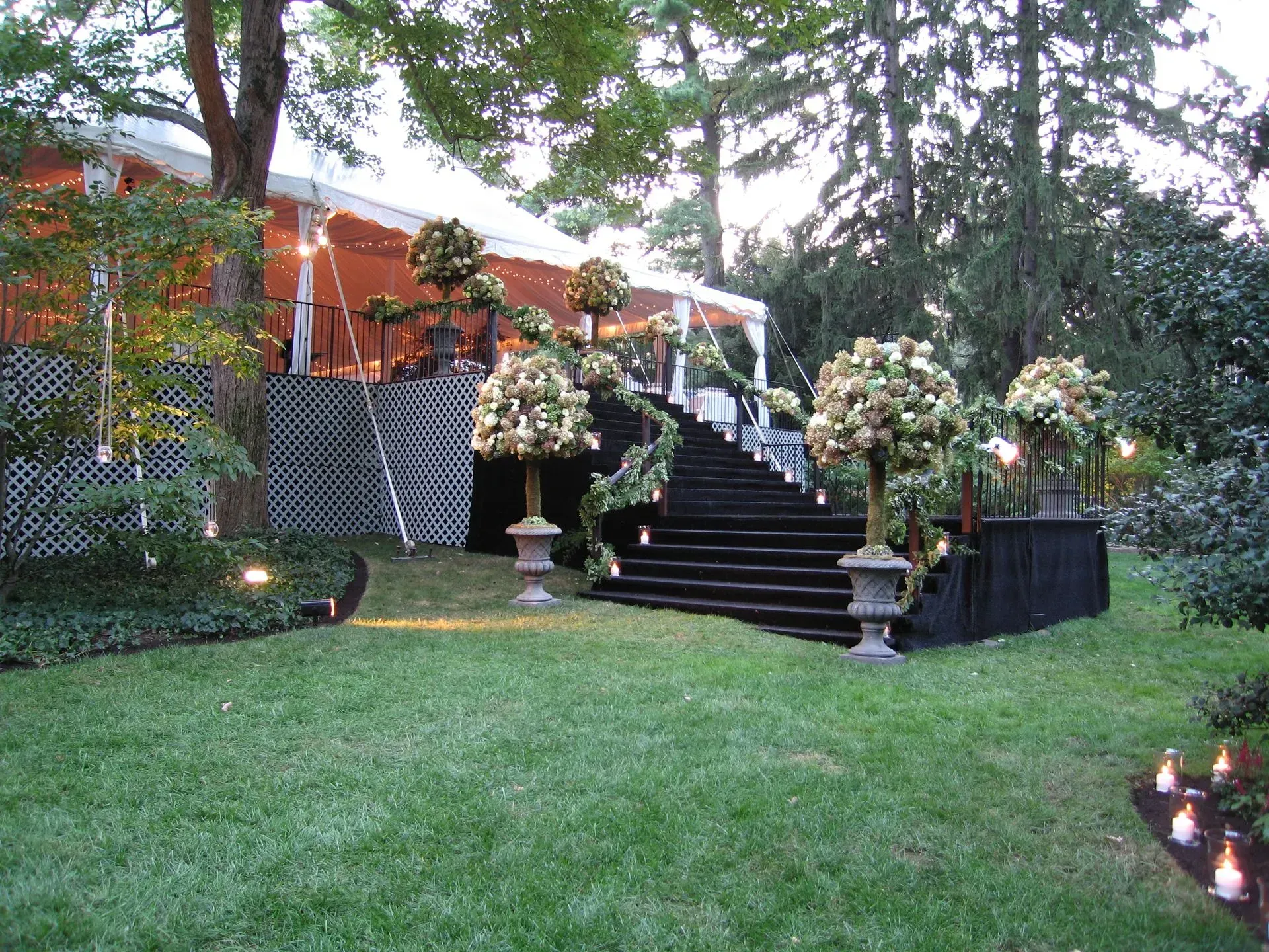A white tent with black stairs leads to a wedding entrance decorated with large floral arrangements and greenery.