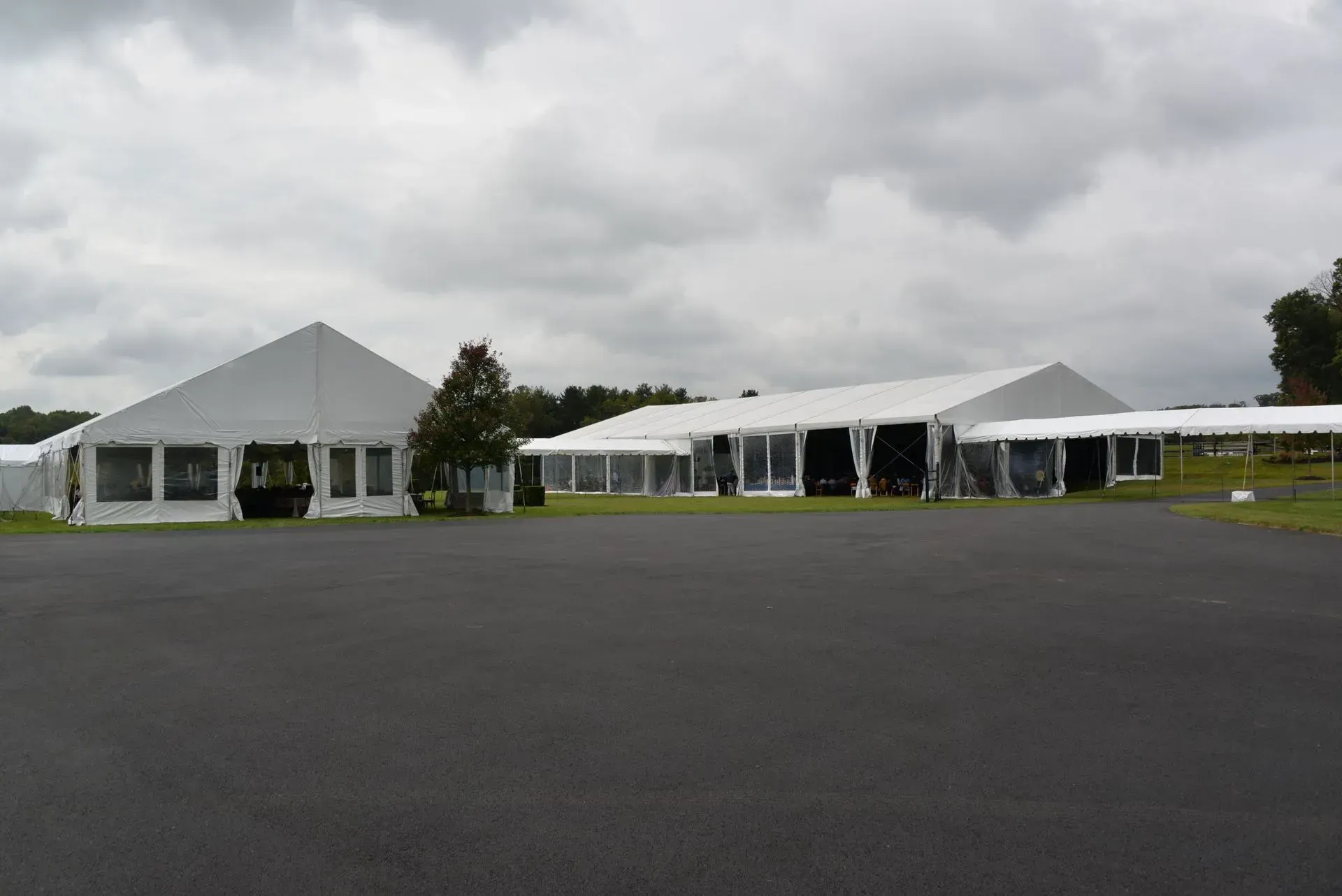 Large white event tents set up on a paved surface under a cloudy sky.