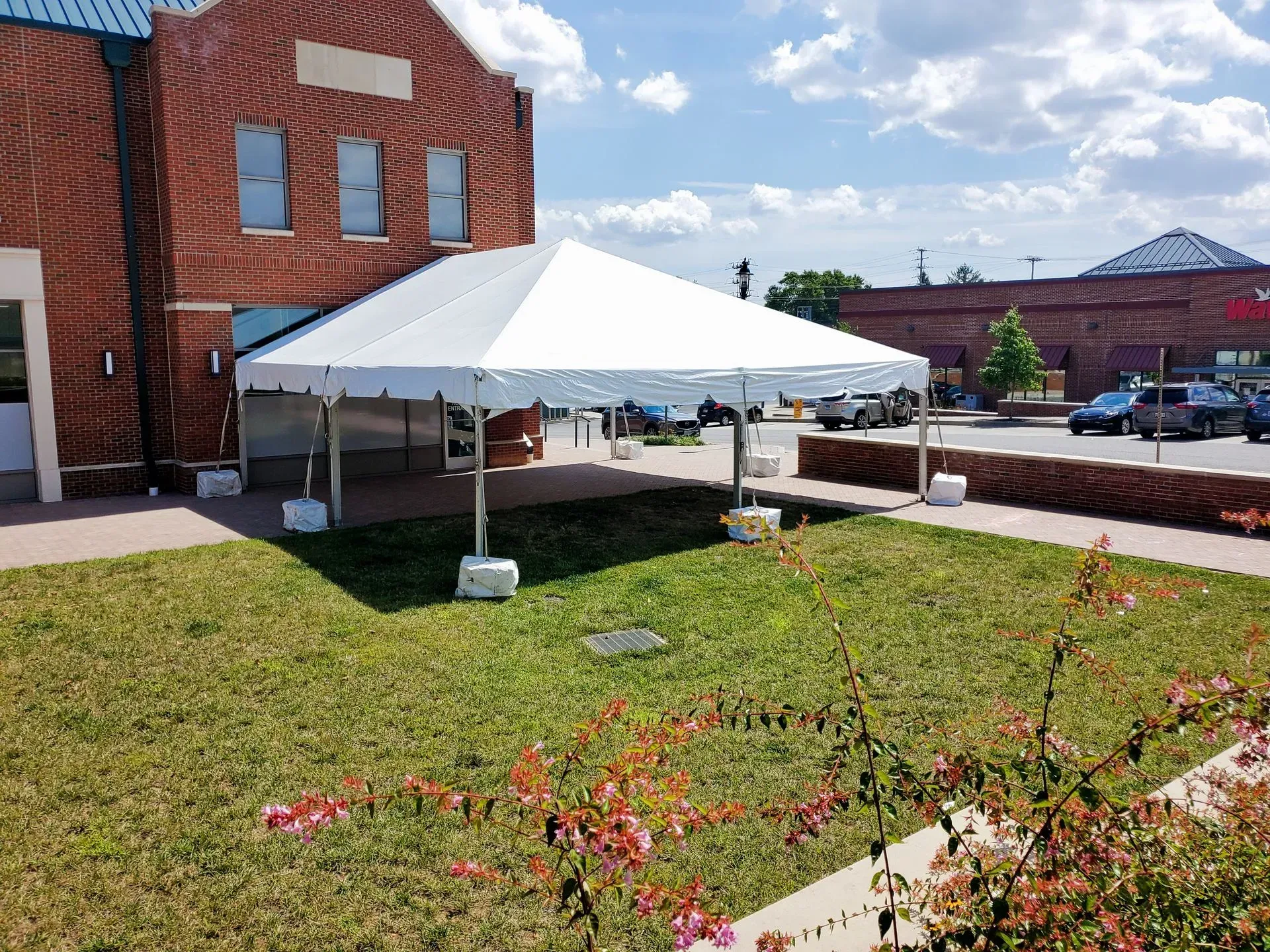 A white event tent stands on a grassy lawn in front of a red brick building on a sunny day.