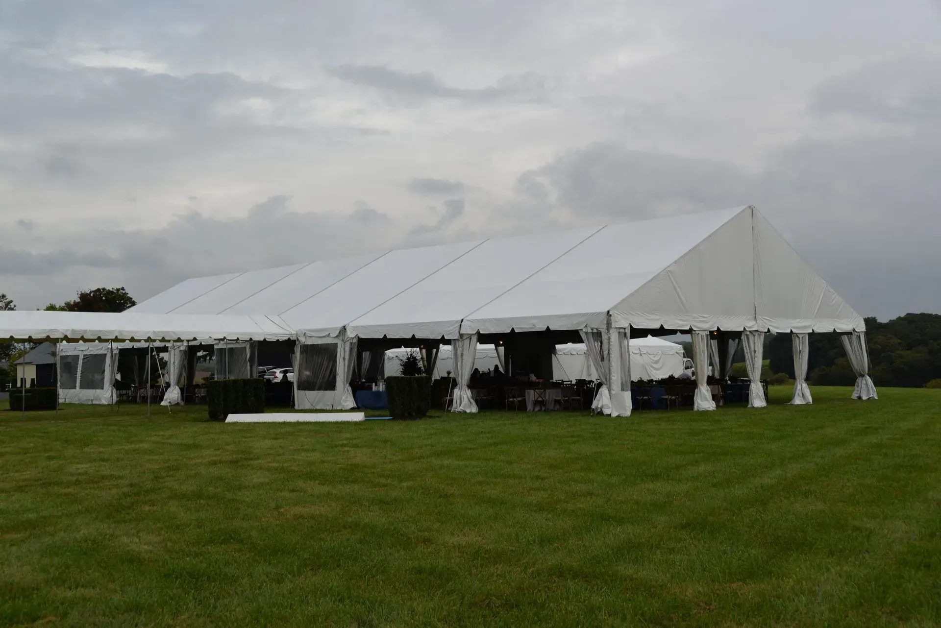 A large white marquee tent with open sides standing in a grassy field under a cloudy sky.