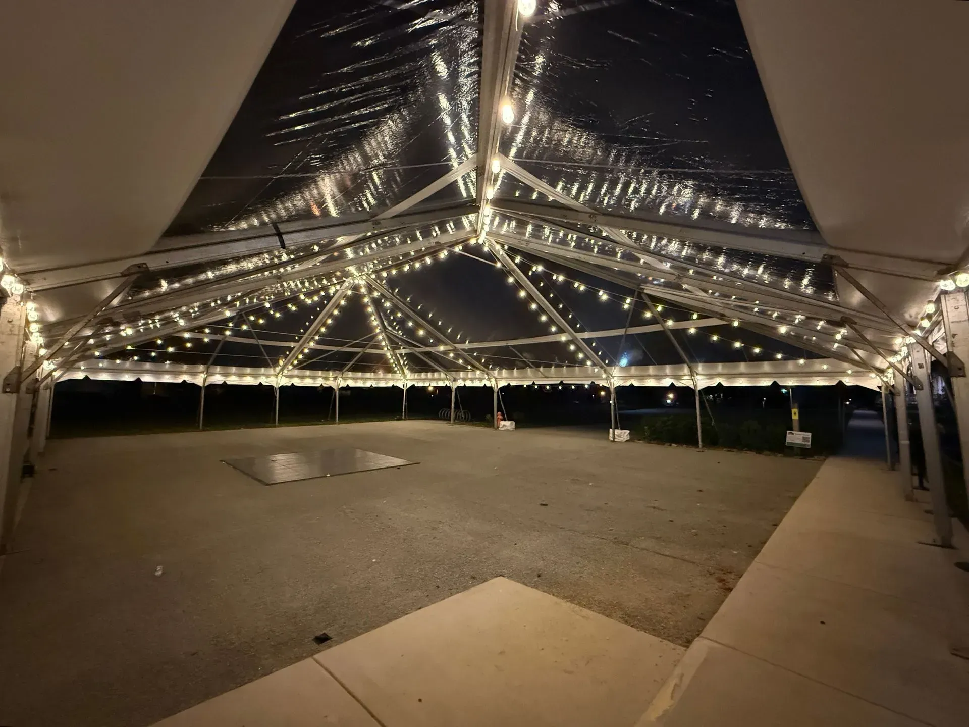 A large, empty event tent at night, featuring a transparent ceiling adorned with strings of warm, glowing fairy lights.