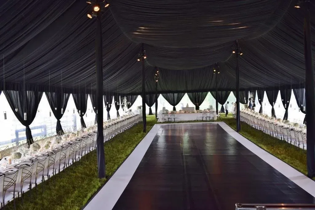 An elegant marquee with a long central dance floor, flanked by rows of white-covered tables under draped black fabric.