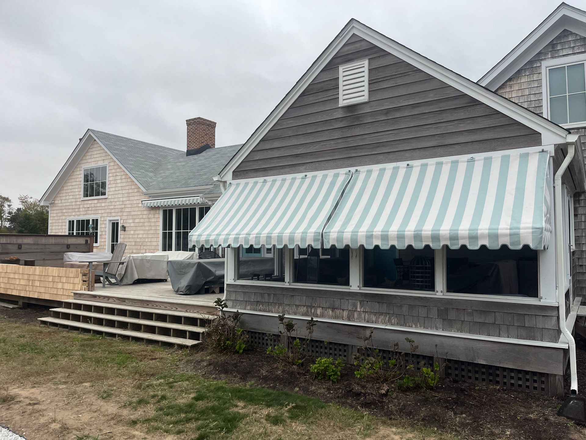 Gray beach house with mint-striped awning, deck, and cloudy sky
