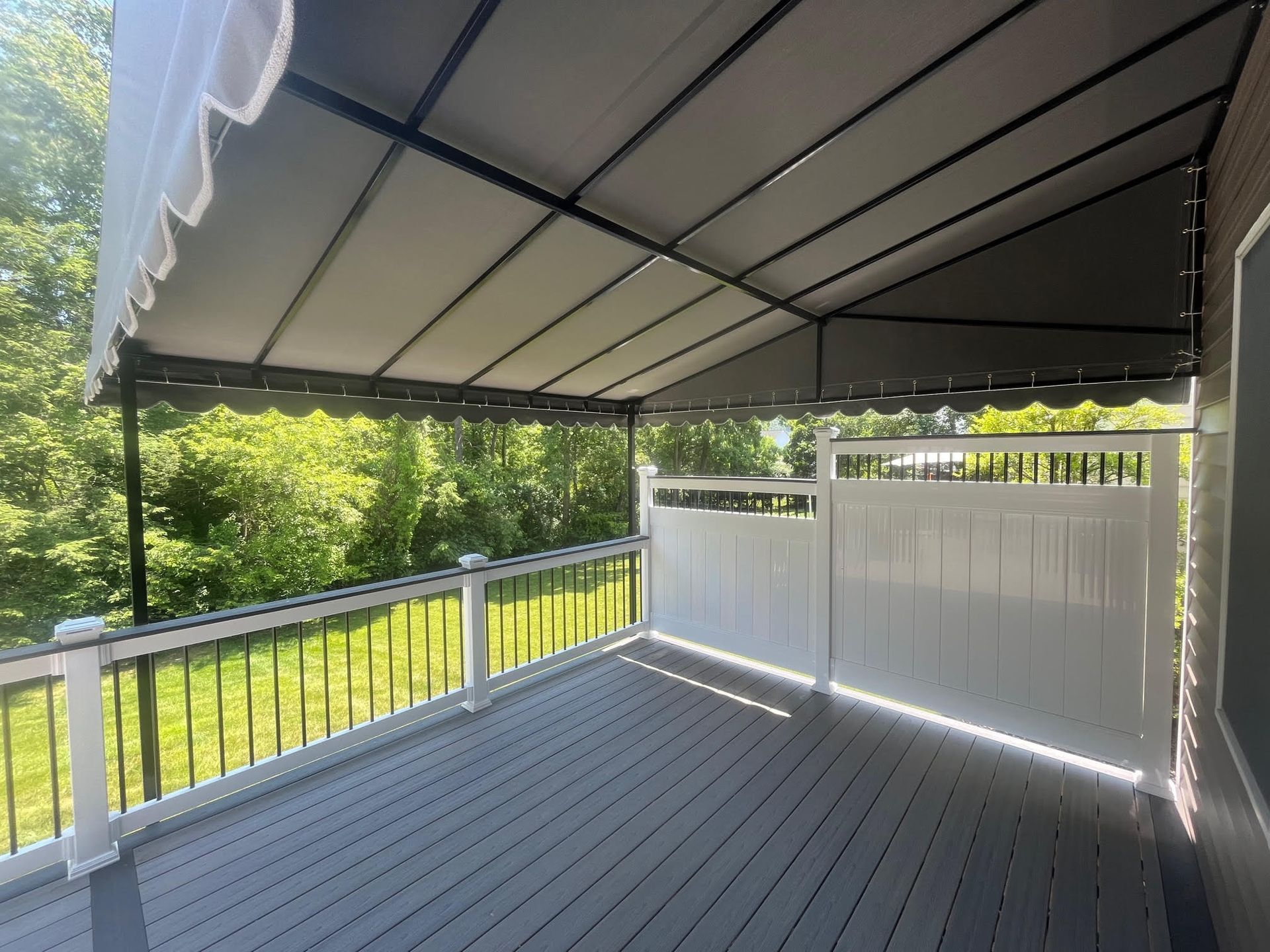Covered wooden deck with white railing and black roof overlooking green yard