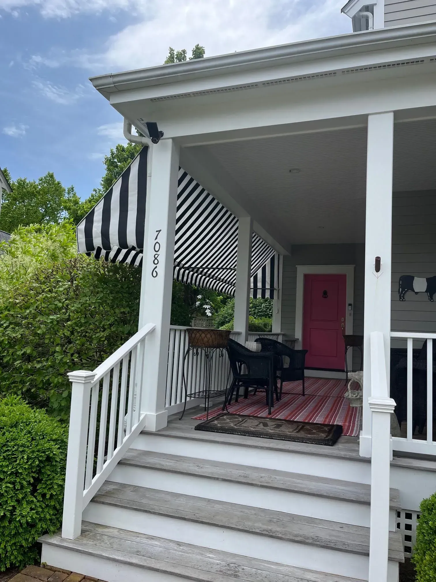 Front porch of a house with white railings, striped black and white awning, and a pink front door.