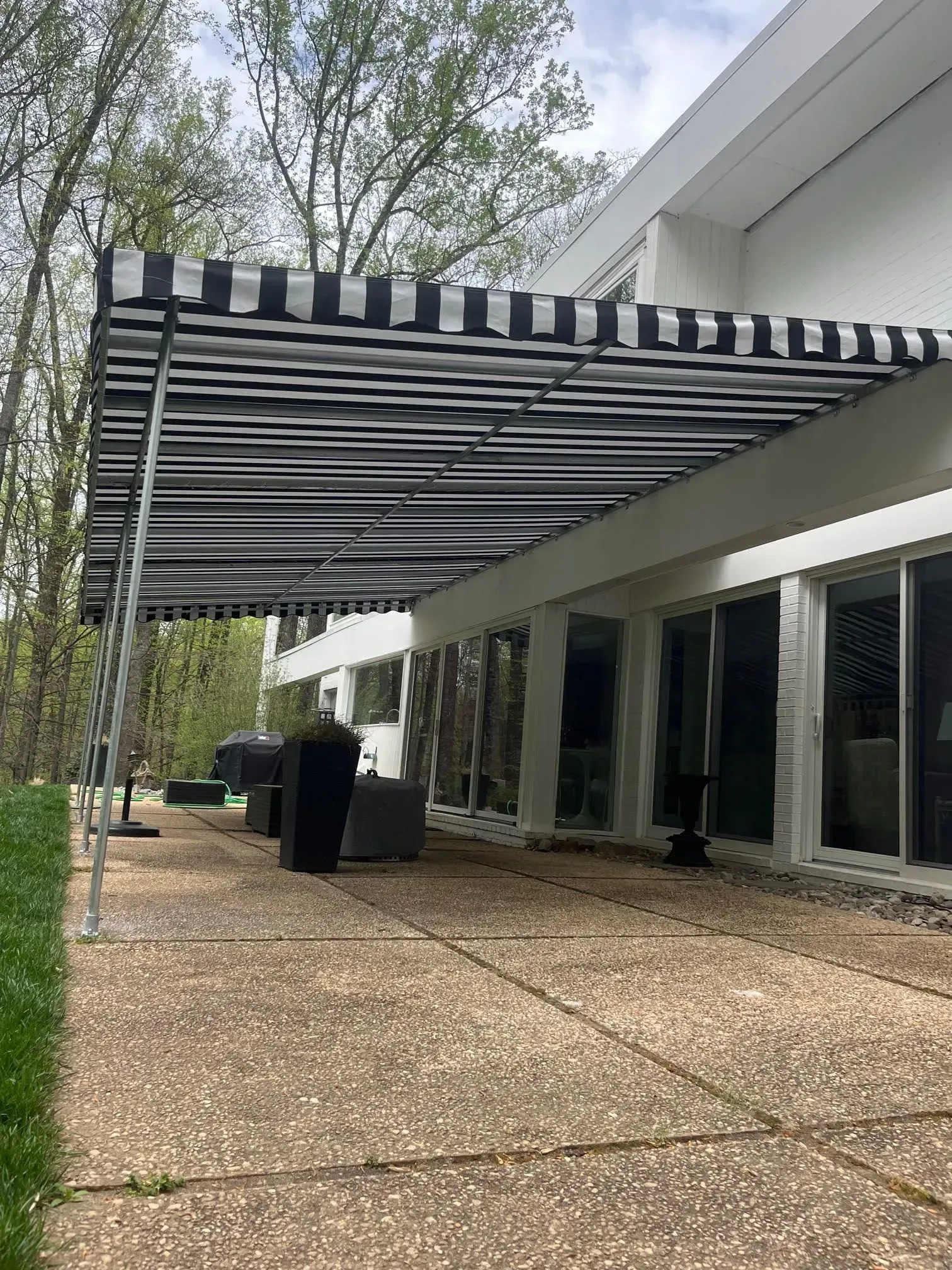 A black-and-white striped awning extends over a stone patio alongside a white building with sliding glass doors.