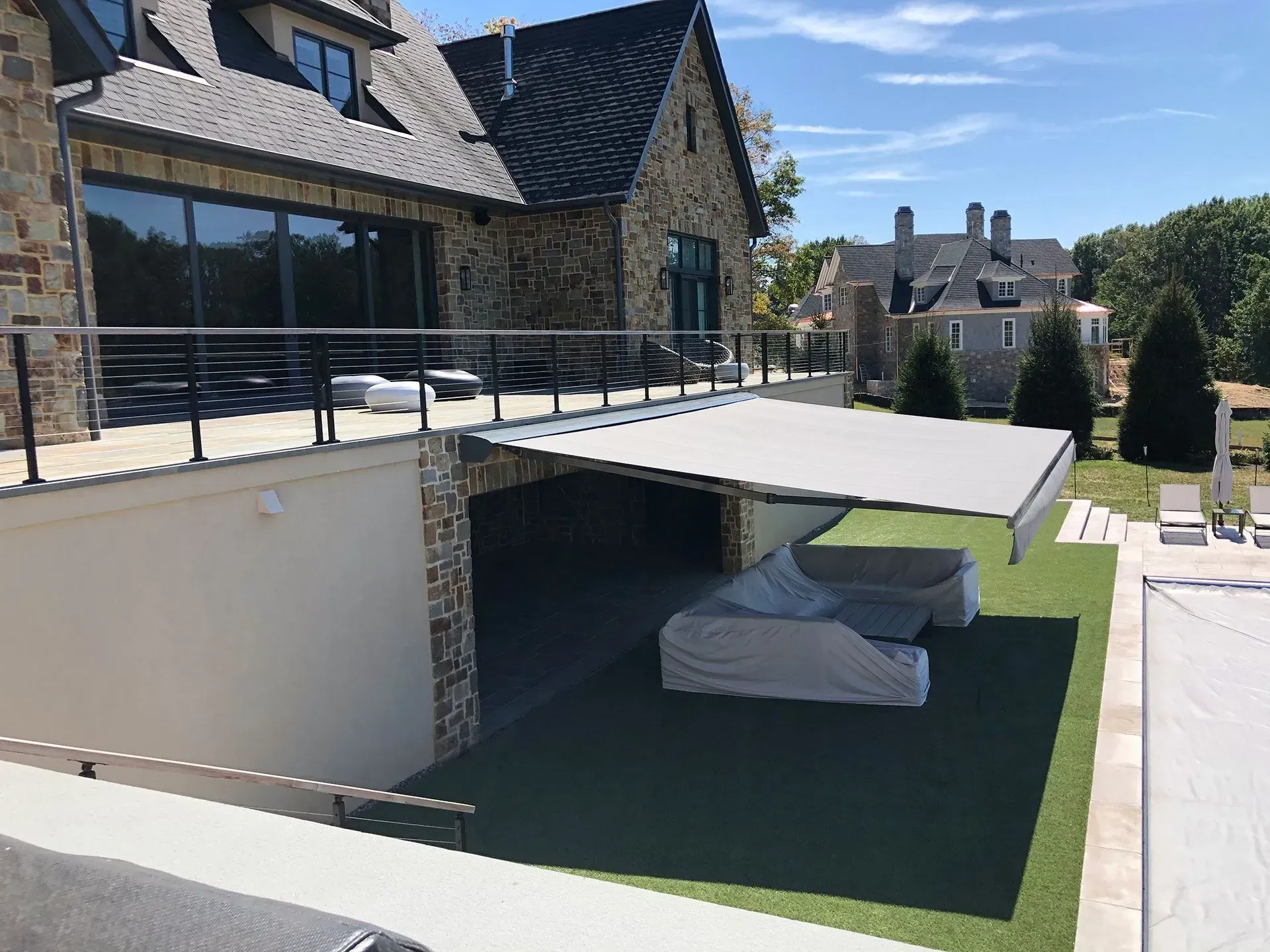 A patio with a retractable awning extending over a covered outdoor seating area with a sofa, attached to a stone house.