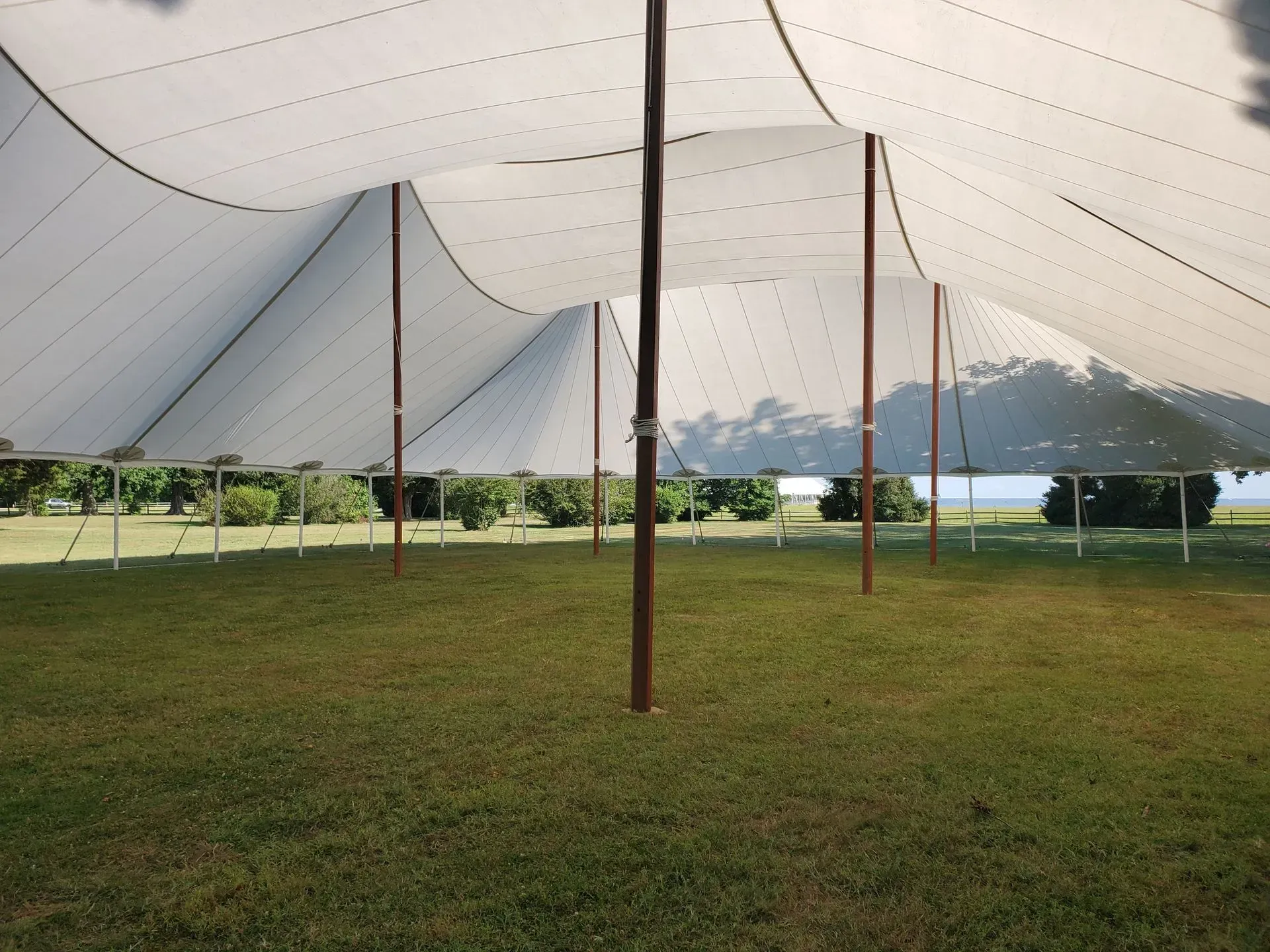 Interior of a large white pole tent set up on a grassy field on a sunny day.