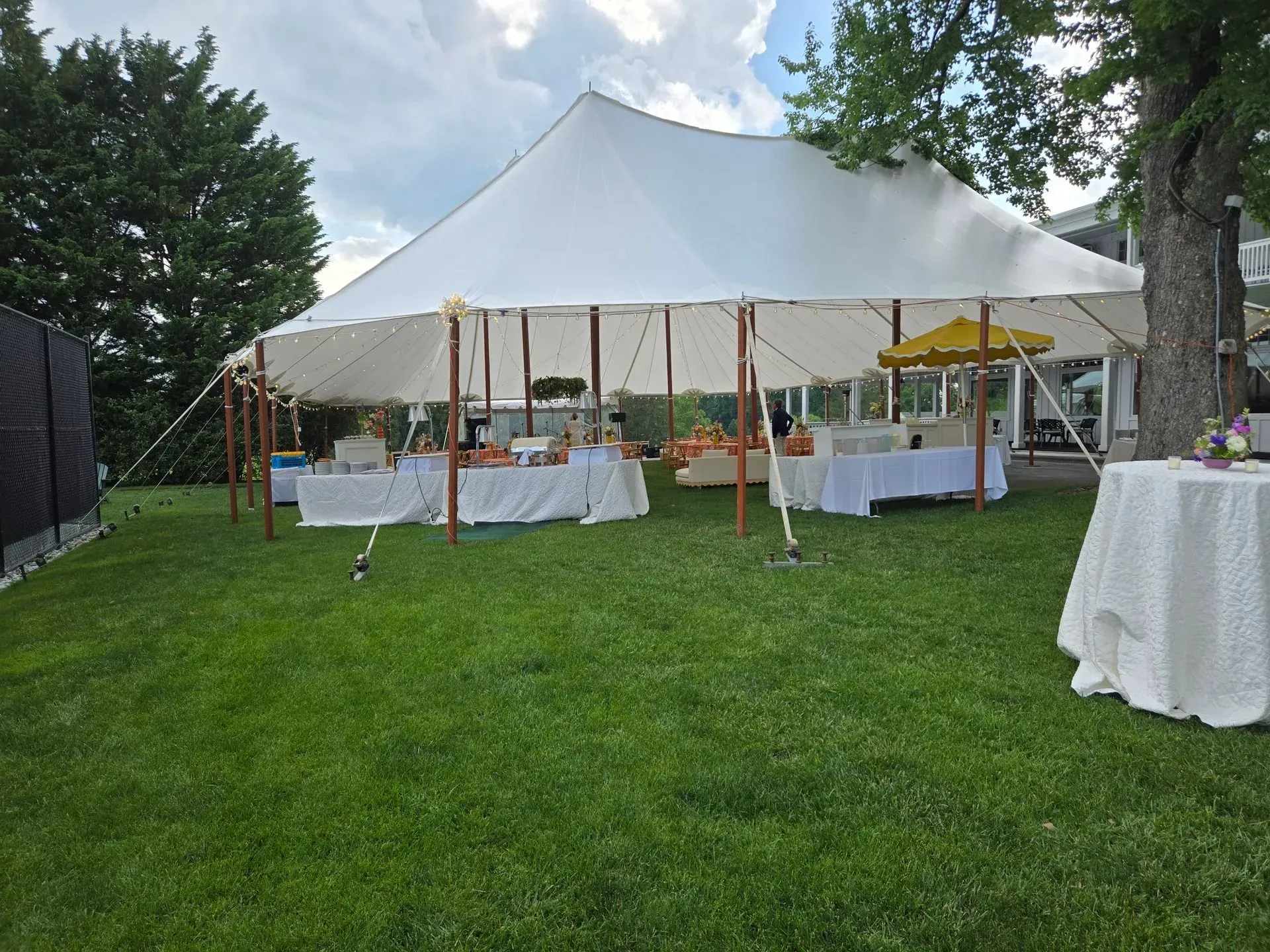 A large white event tent set up on a green lawn with tables underneath and a smaller, separate table in the foreground.