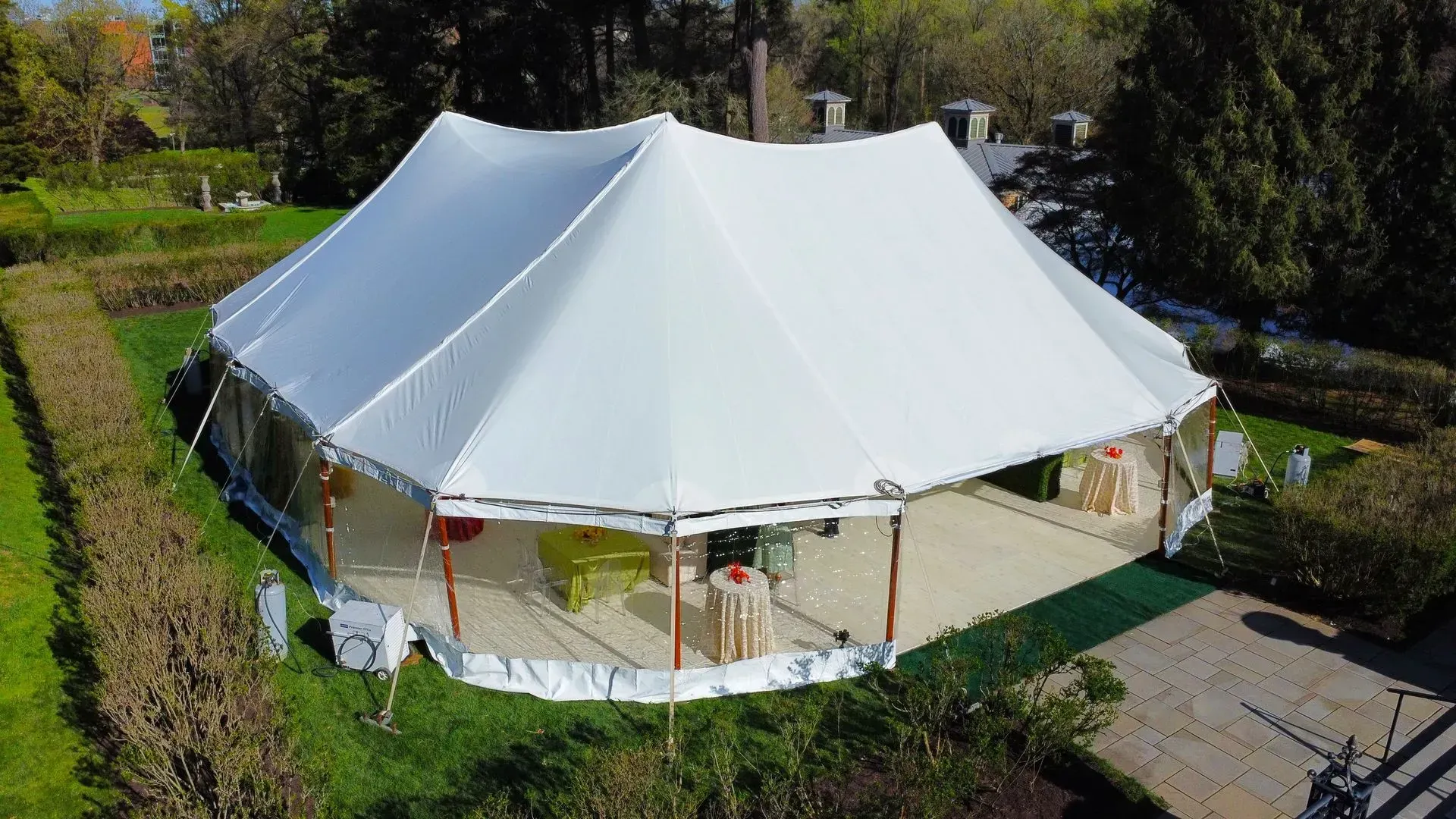 A large white pole tent set up on a grassy lawn with trees in the background.