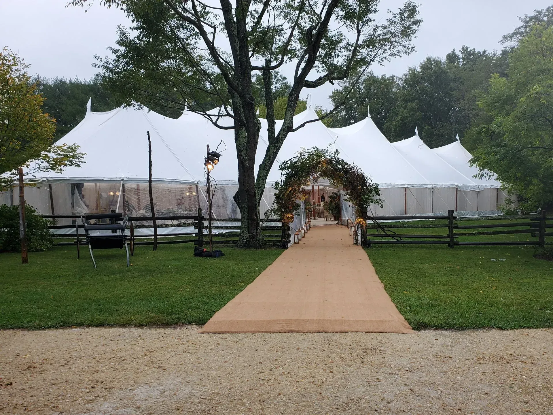 A long white event tent set up in a grassy area with a floral archway leading to the entrance over a tan pathway.