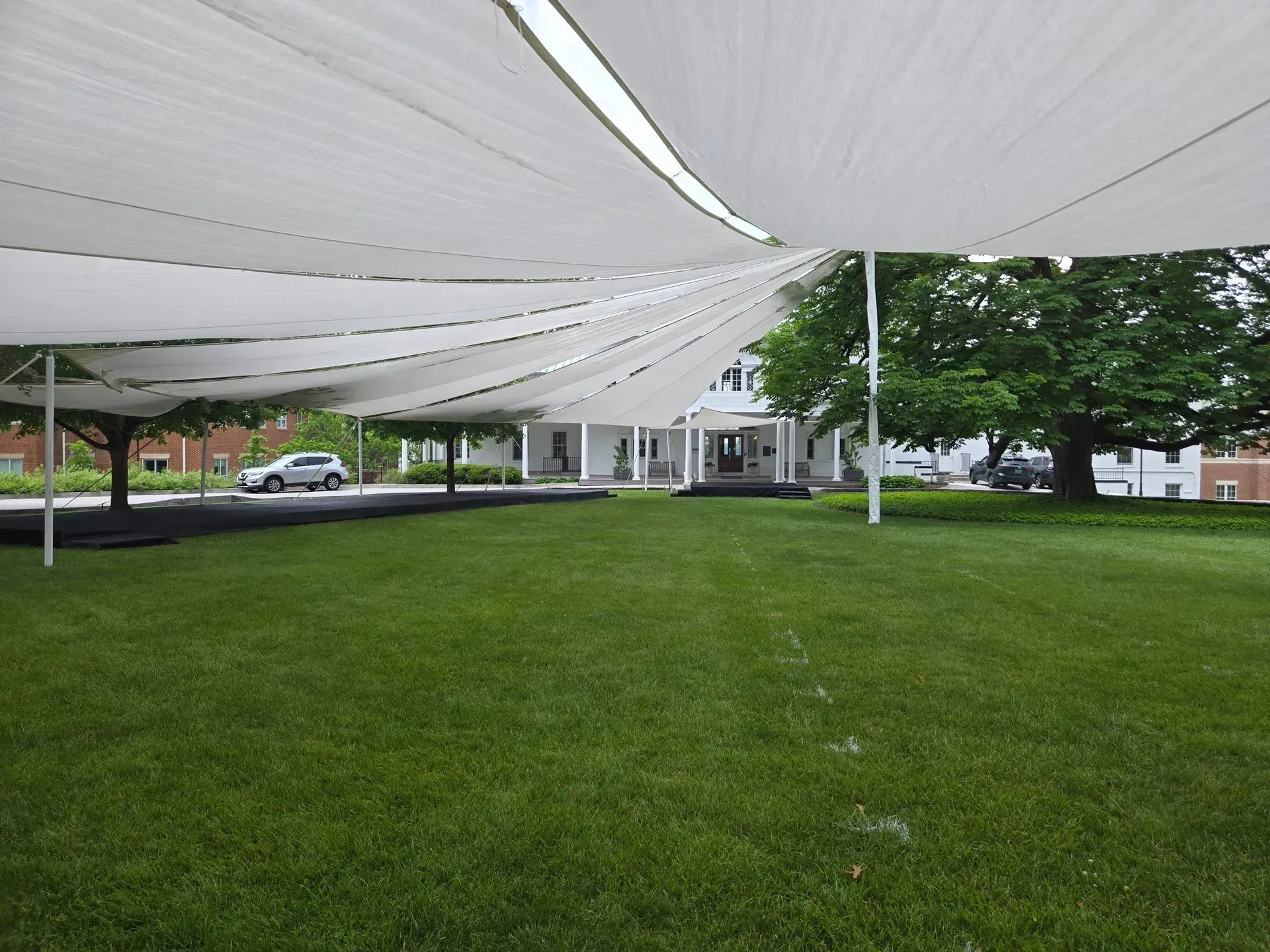 White shade sails stretched over a grassy lawn in front of a white building with a porch and mature trees.