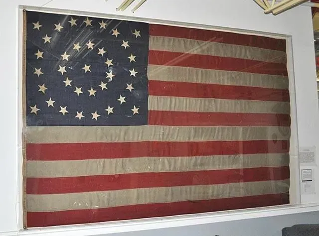 A framed, vintage American flag with stars arranged in a circle pattern against a blue field, mounted on a white wall.