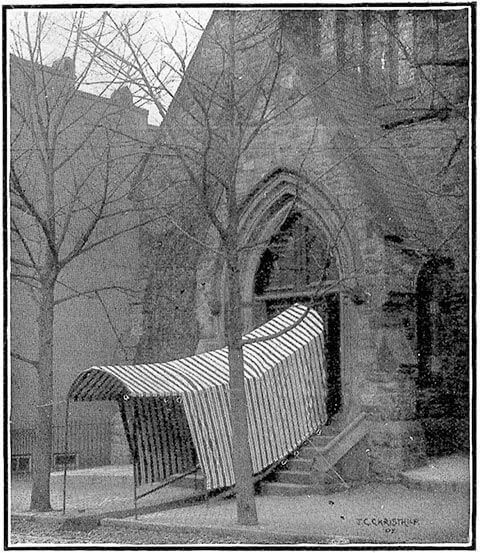 A black-and-white photo shows a striped, temporary canopy extending from the arched doorway of a stone church building.
