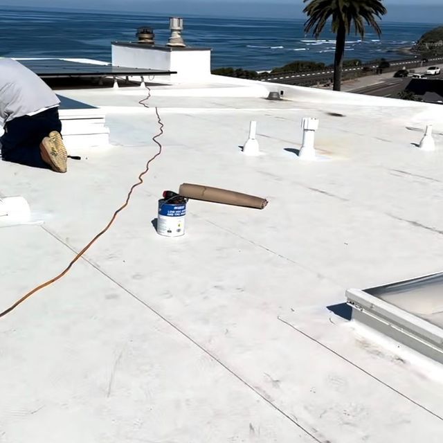 A man is working on a white roof with the ocean in the background