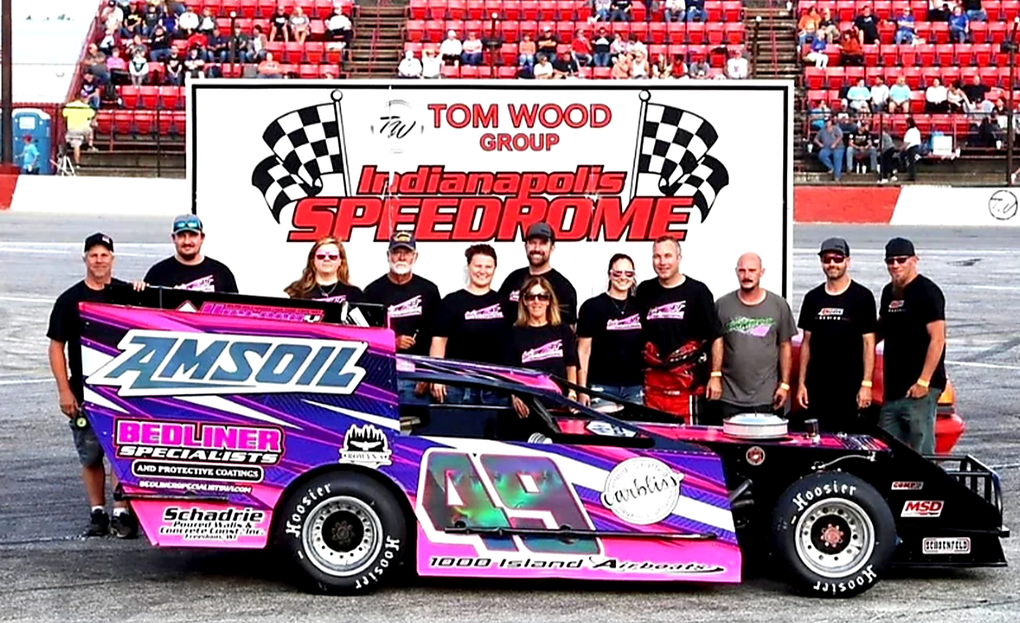 Race car and team posed at a racetrack.