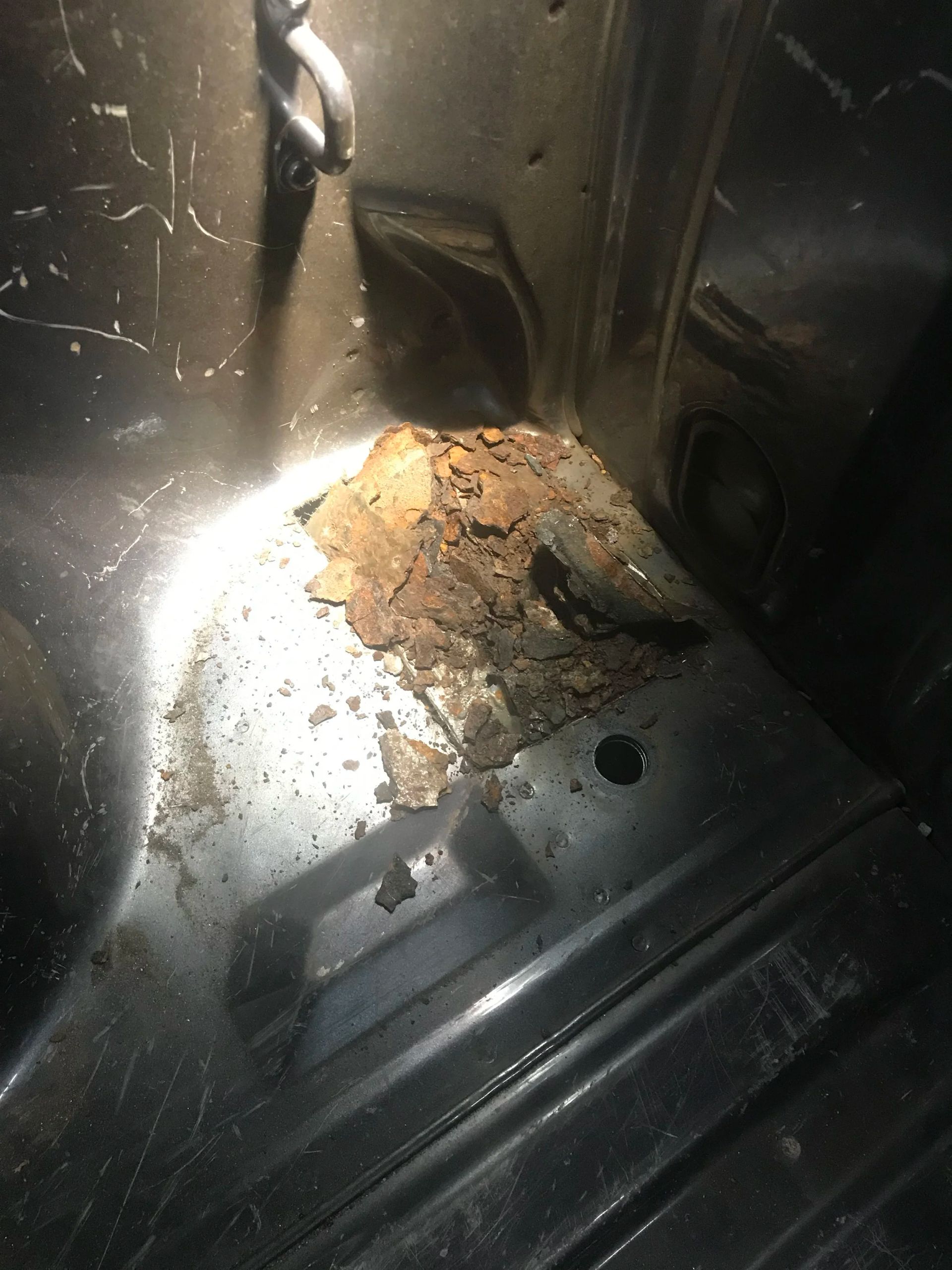 Close-up of rusty debris or corrosion inside a metal compartment, lit by a bright flashlight.
