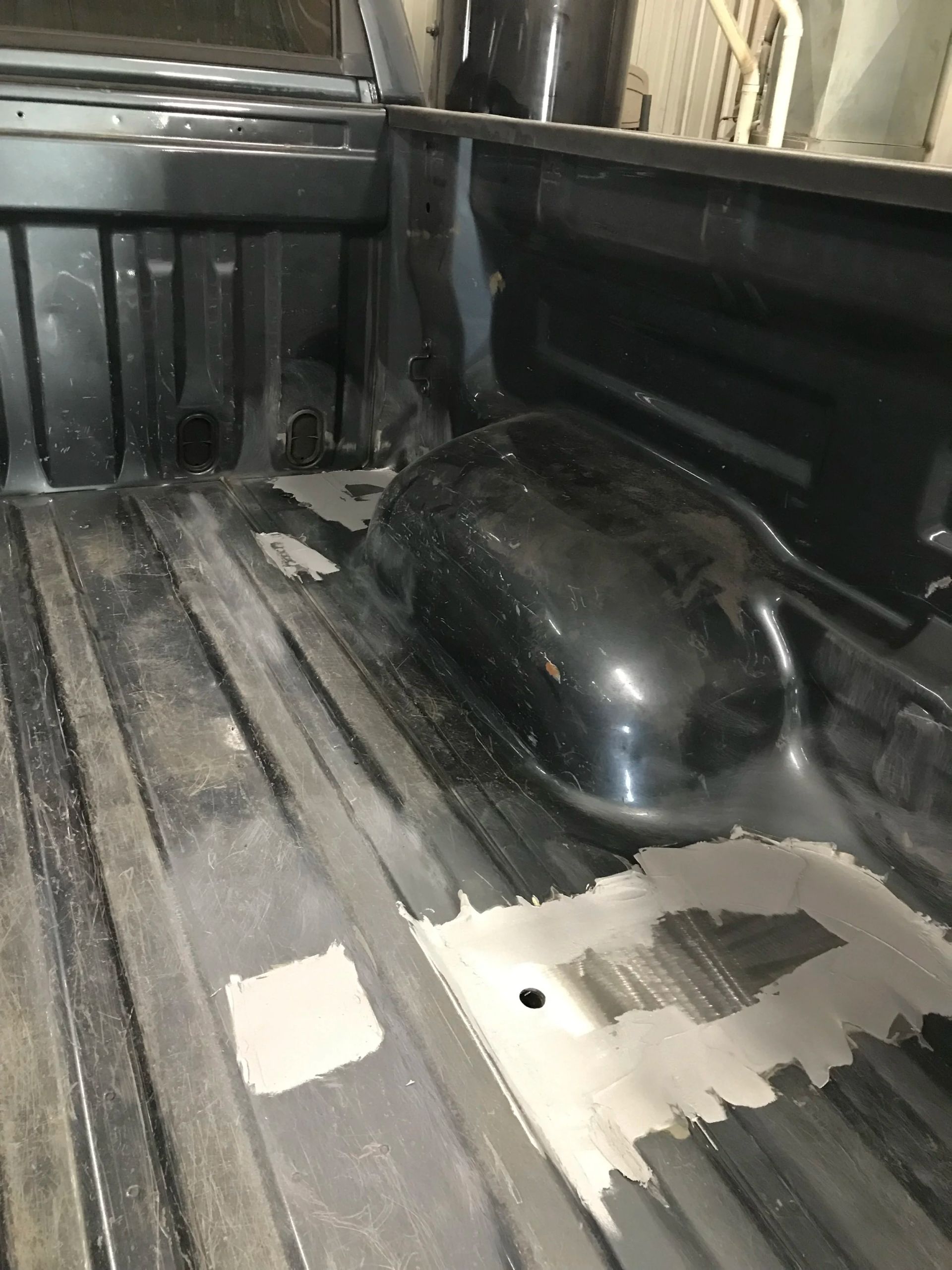 Dirty pickup truck bed with a black wheel well cover and peeling paint.