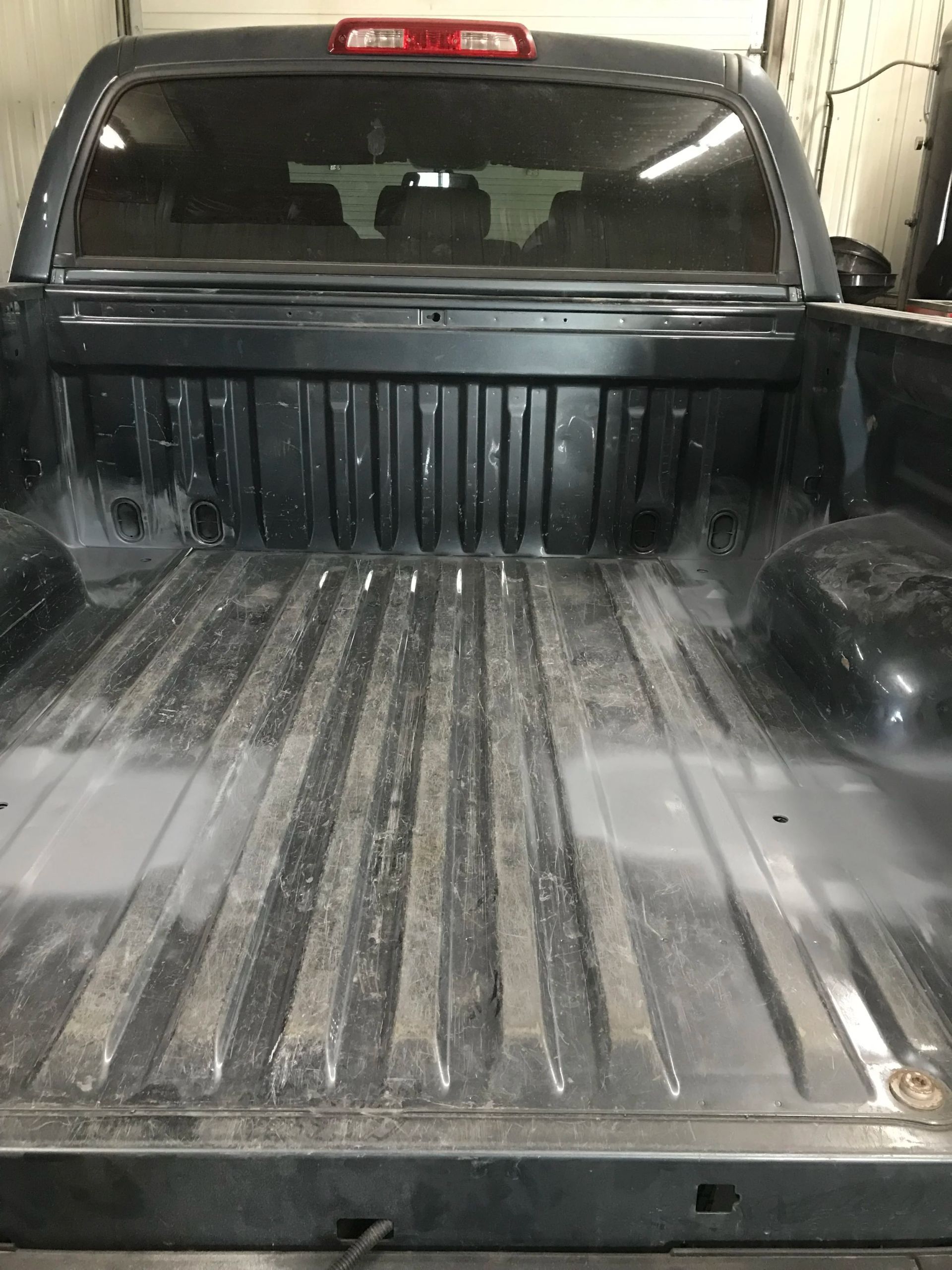 Empty black pickup truck bed viewed from the tailgate, with red cab brake light visible.