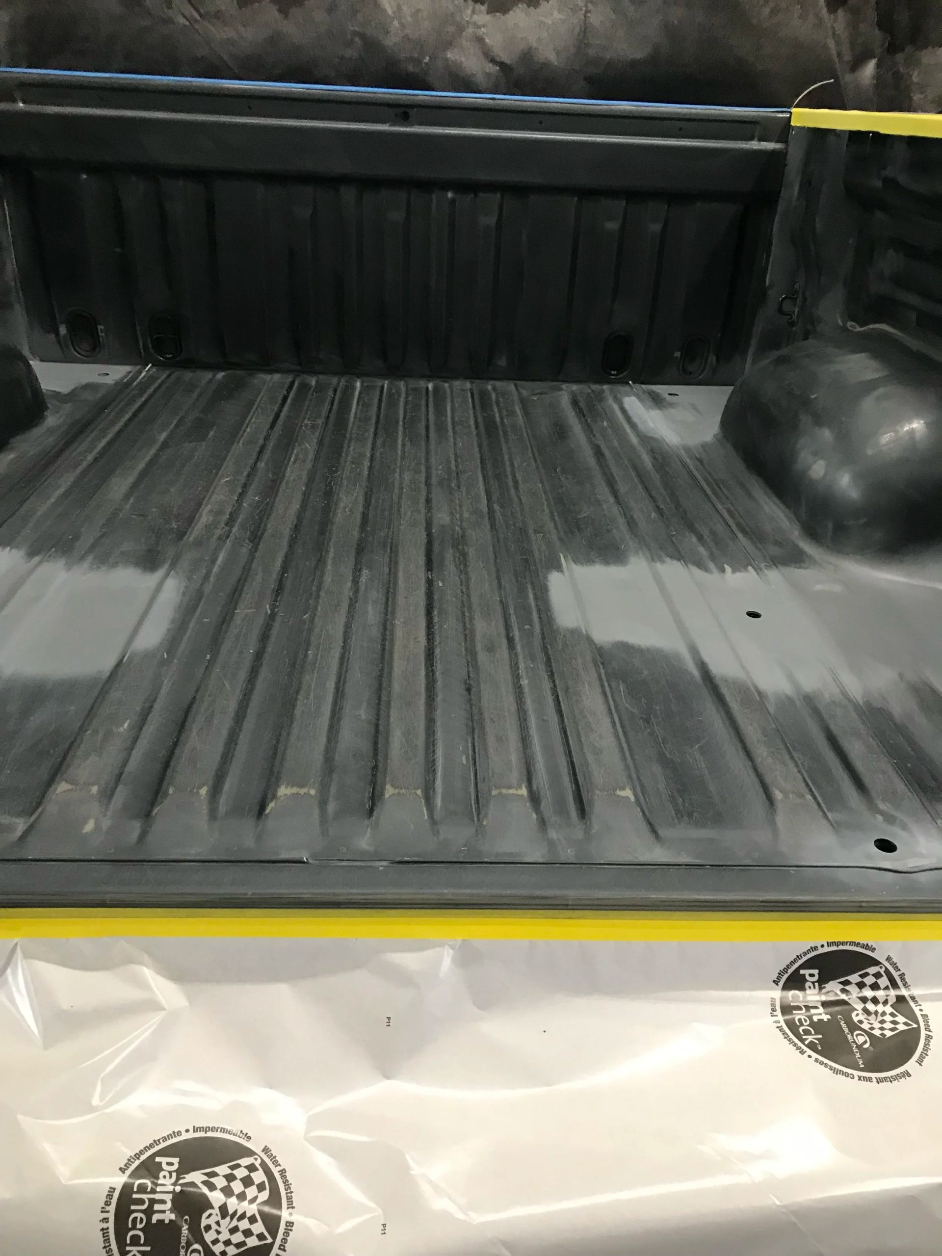 Empty black truck bed with a ribbed floor and white tailgate edge.