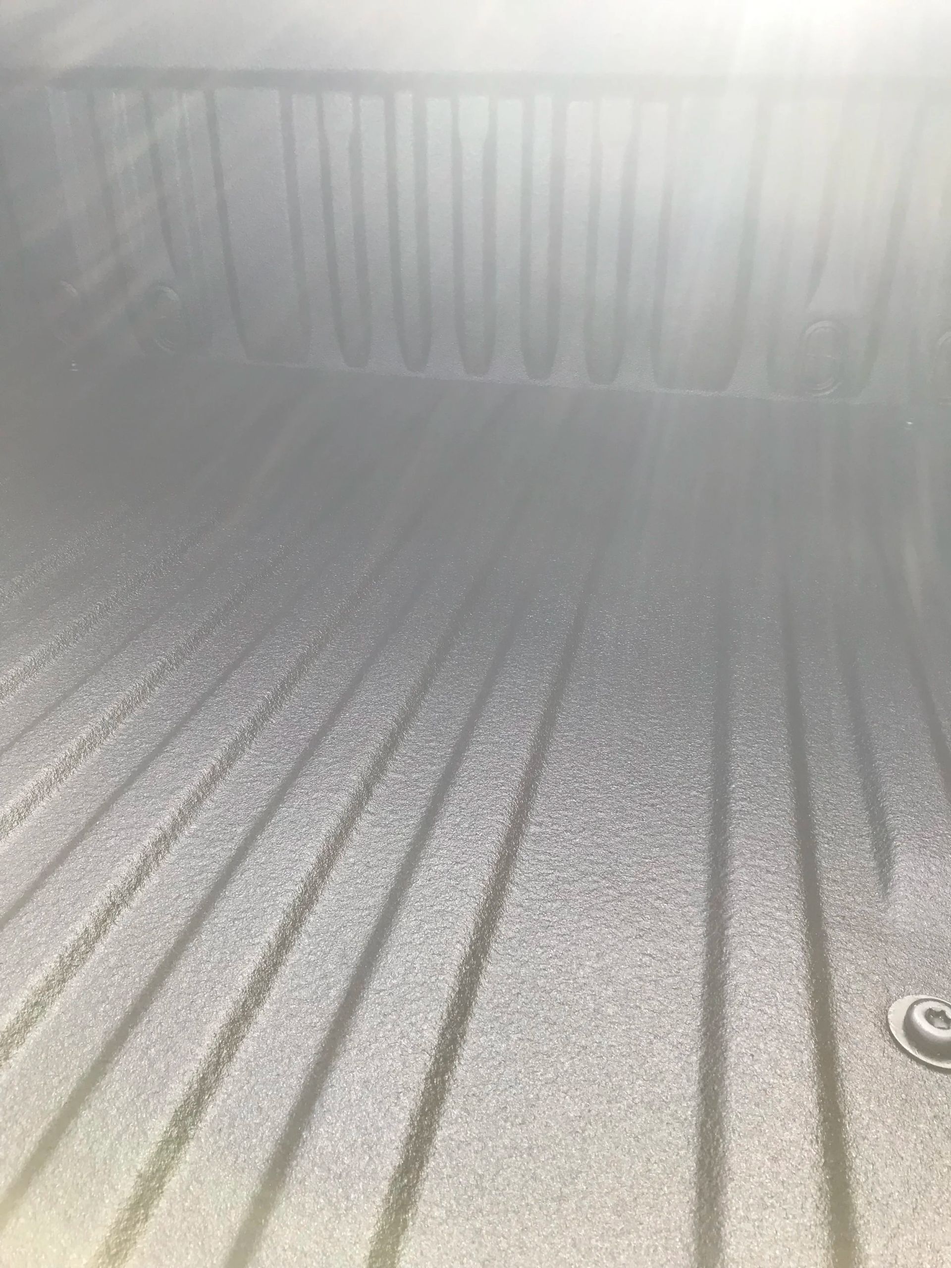 Empty metallic pickup truck bed with textured gray liner and a drain hole in the corner