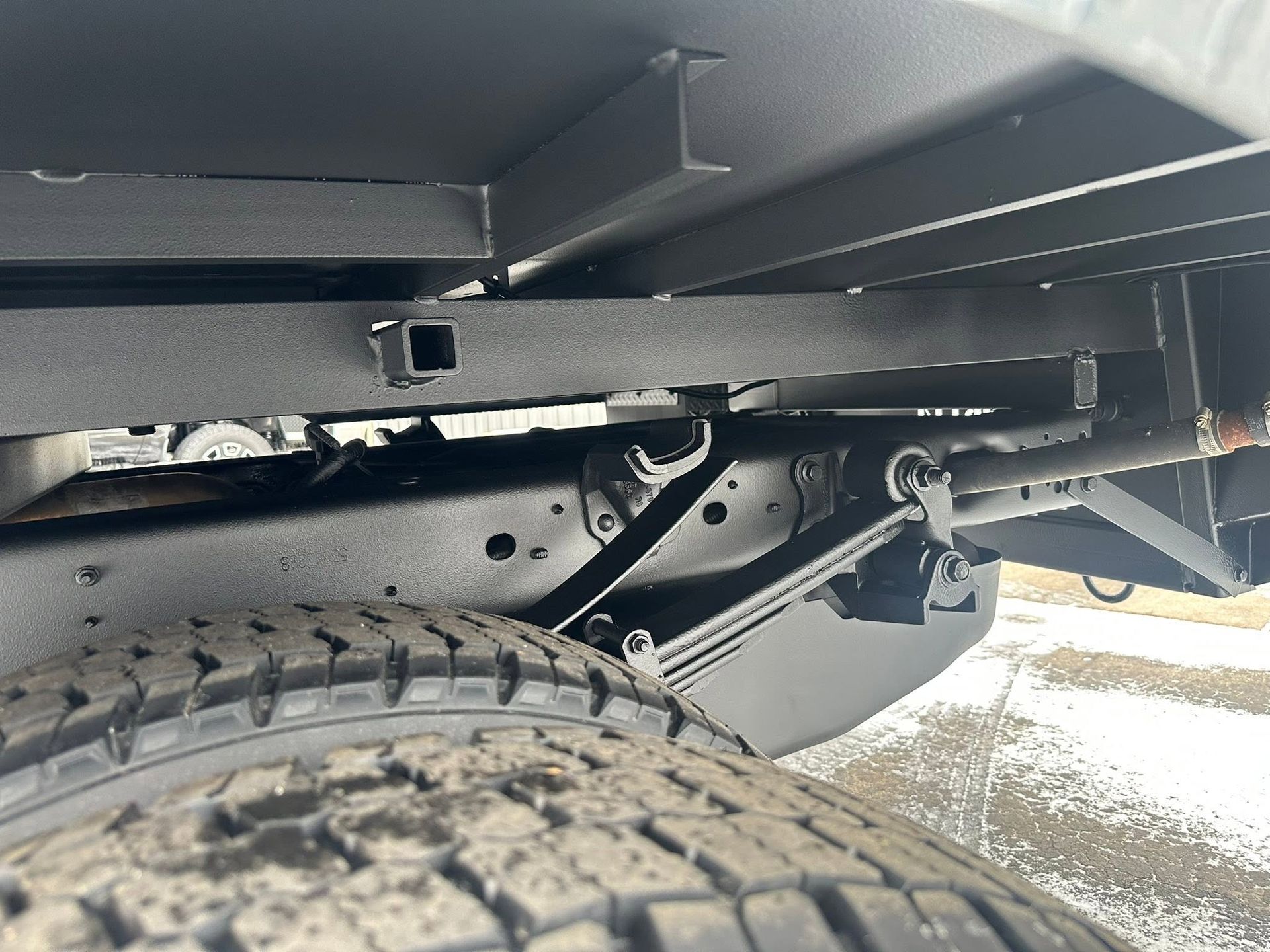 Close-up of a vehicle’s rear wheel and undercarriage with black suspension parts and snow on the ground