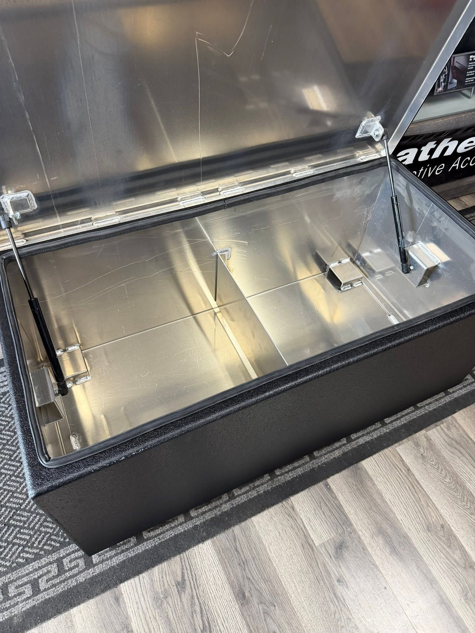 Open metal storage case with a reflective lid and a few small hardware pieces inside on a carpeted floor