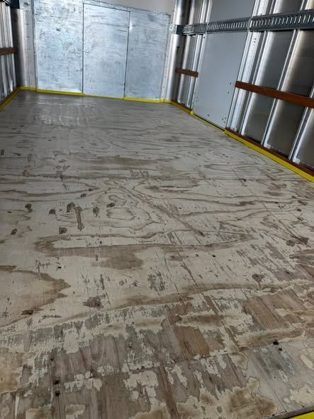 Empty cargo trailer interior with scuffed wooden floor and silver metal walls