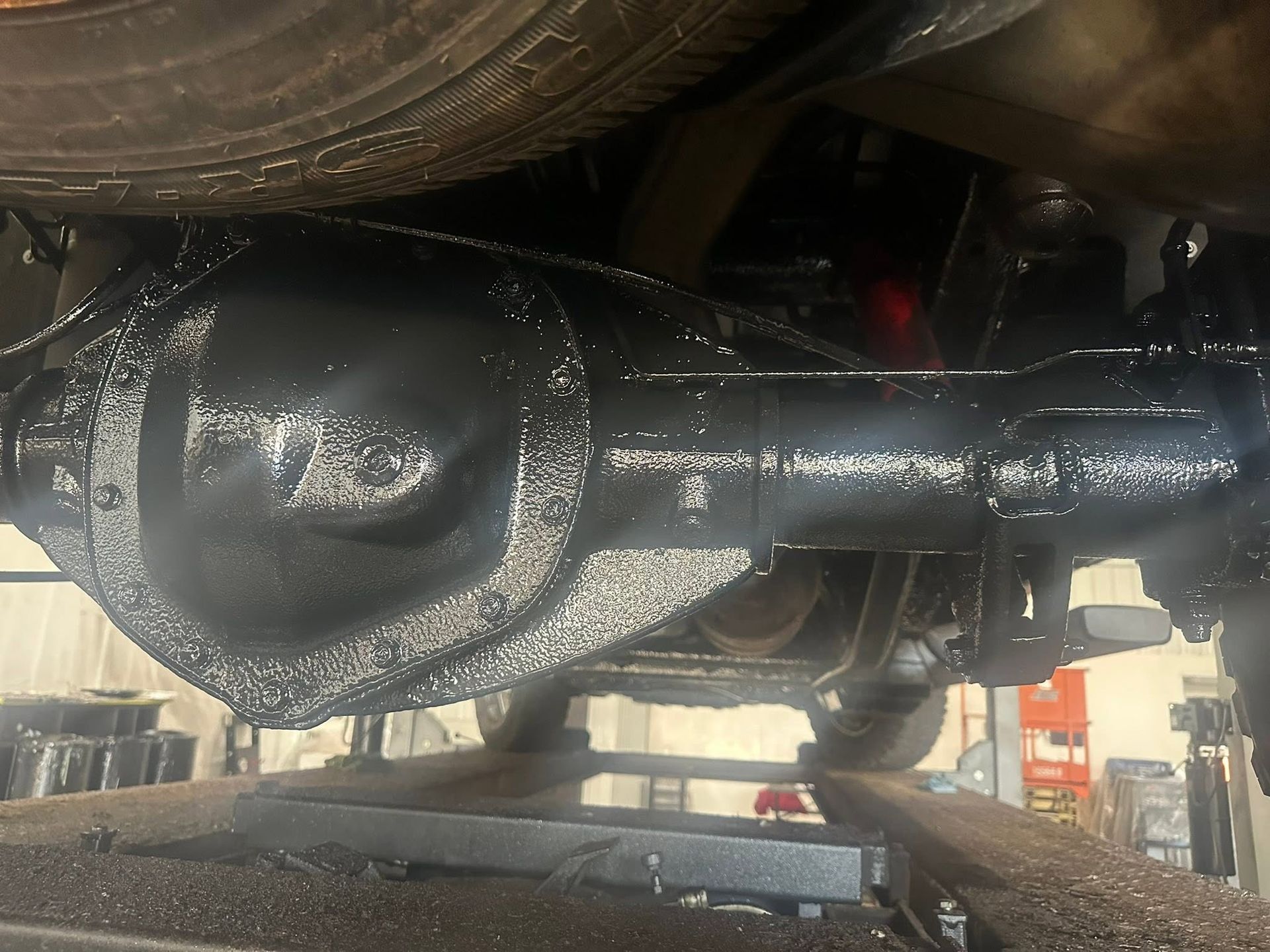 Underneath a vehicle, freshly painted black rear axle and suspension assembly in a garage.