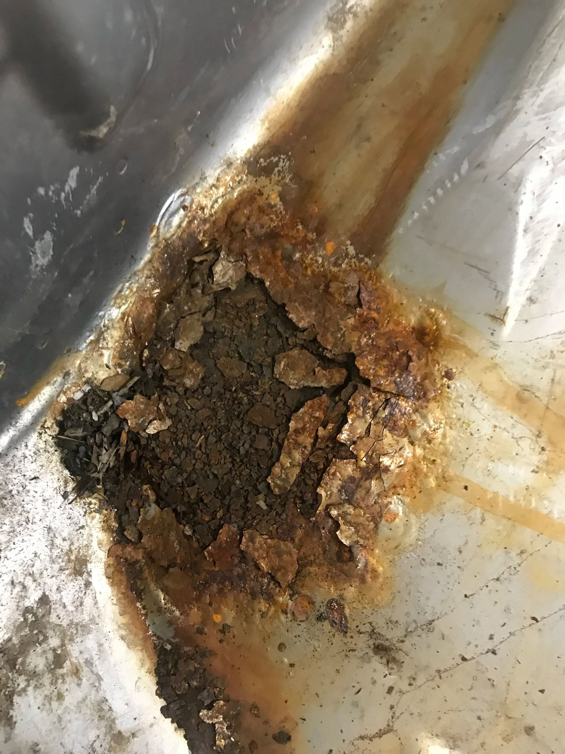 Rusty corroded hole in a metal surface with brown-orange staining and peeling debris