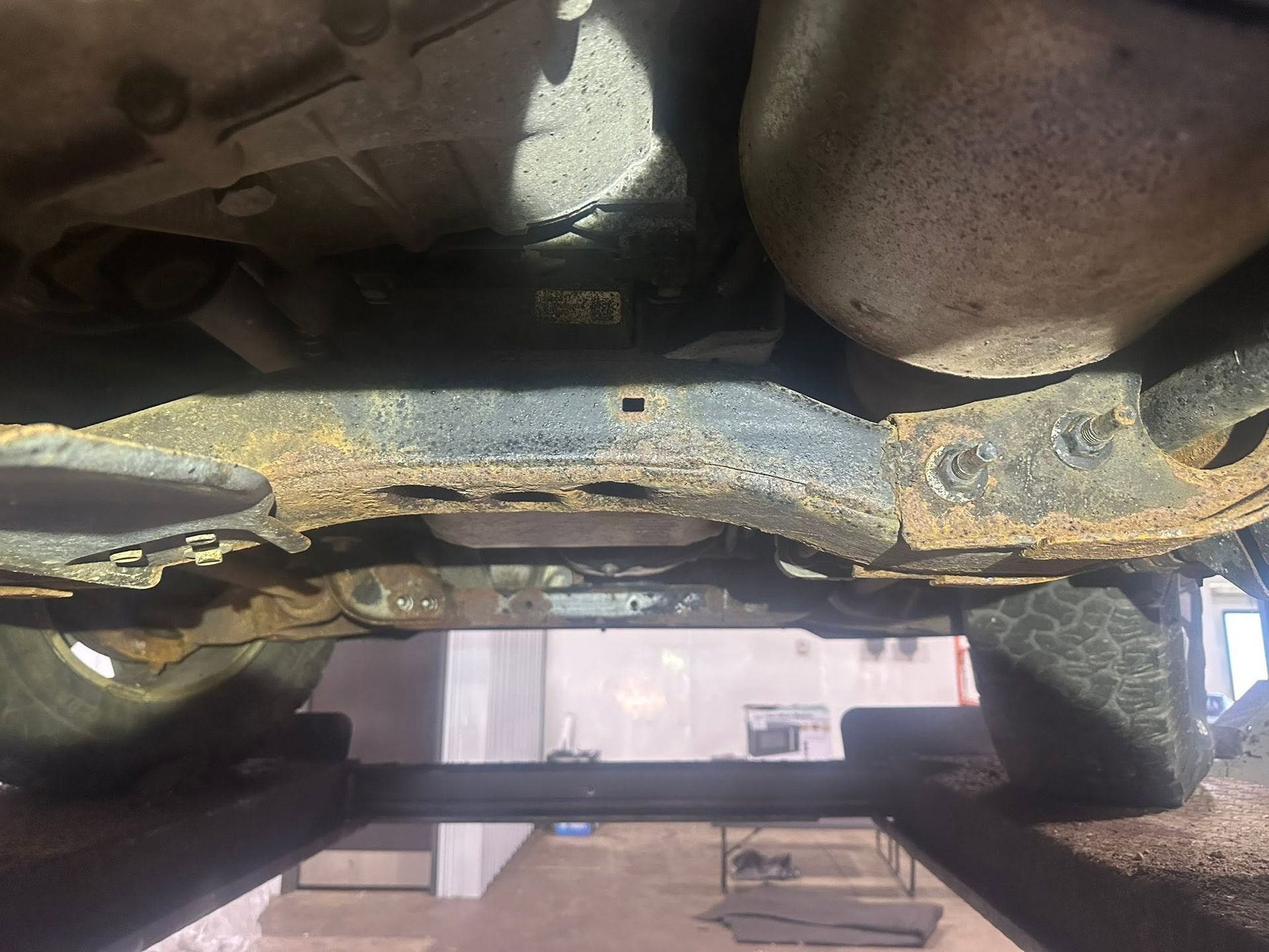 Rusty car undercarriage with corroded metal and a visible exhaust pipe over a lift