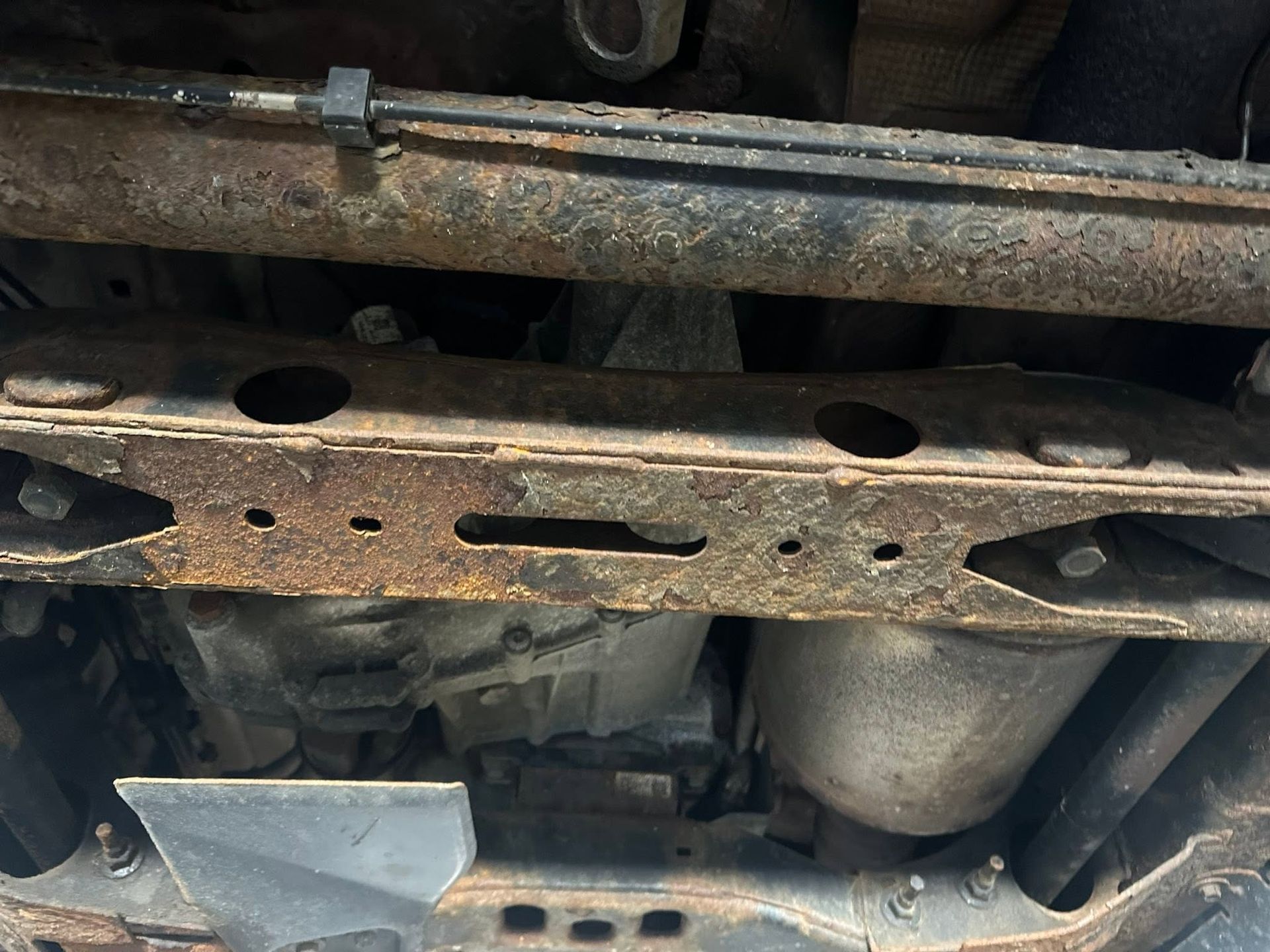 Undercarriage of a vehicle showing rusty metal frame, exhaust pipe, and heat shield underneath.
