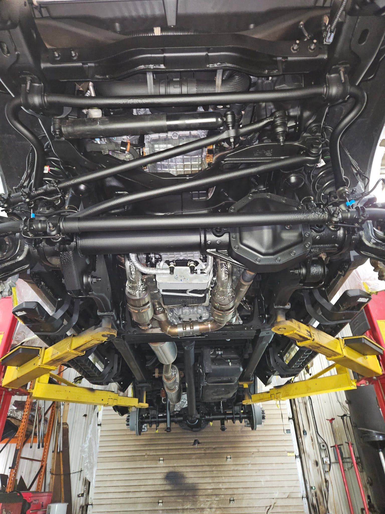 Undercarriage of a vehicle on a lift, showing black suspension bars and yellow support arms.