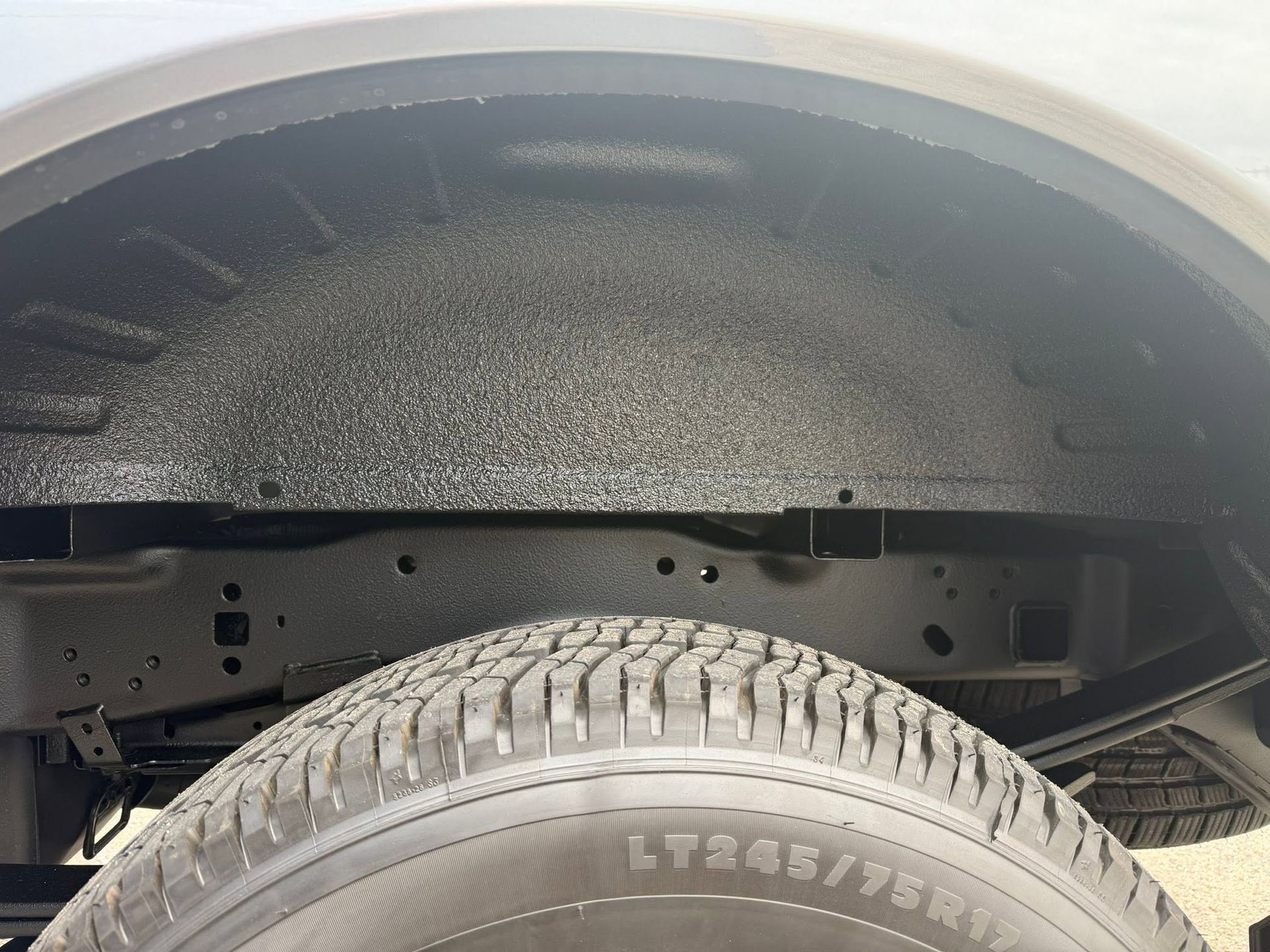 Car wheel and tire under a vehicle, showing the wheel well and suspension area.