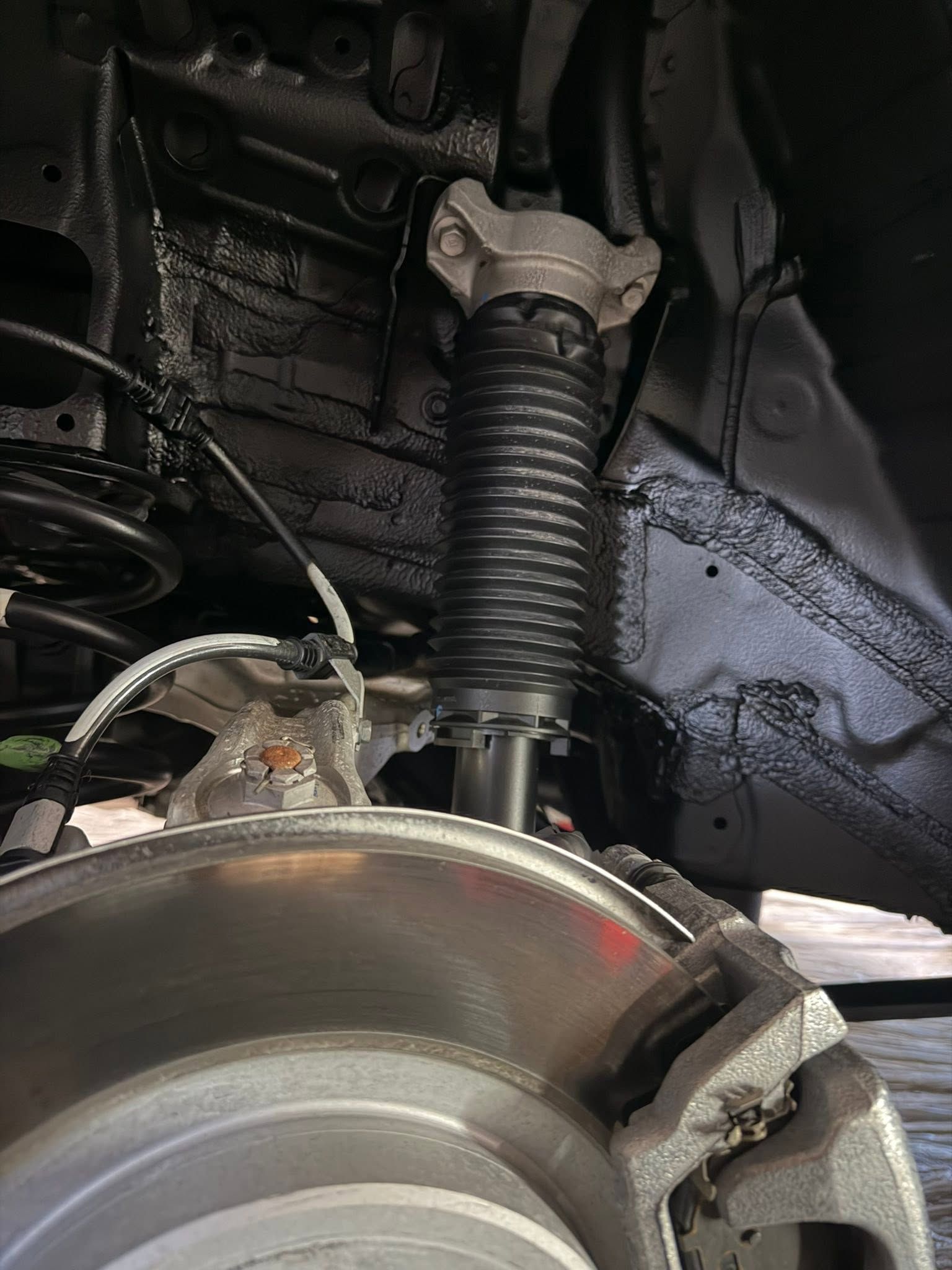 Car wheel and suspension in a wheel well, with brake rotor and dust-covered undercarriage.