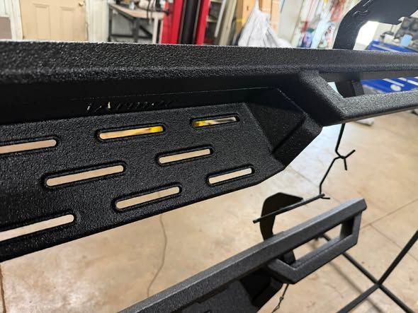 Black metal rack with slotted panels and a hinged bracket, shown close-up on a concrete floor.