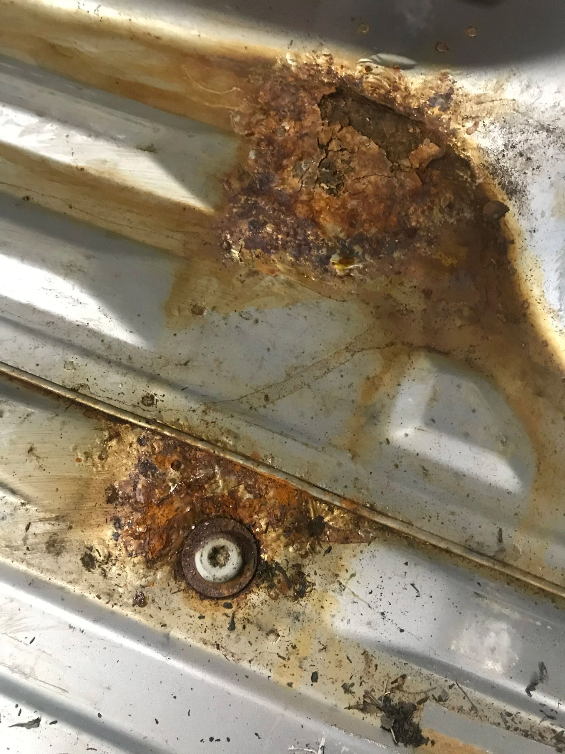 Rusty corroded metal panel with two large rust spots and a bolt near the bottom.