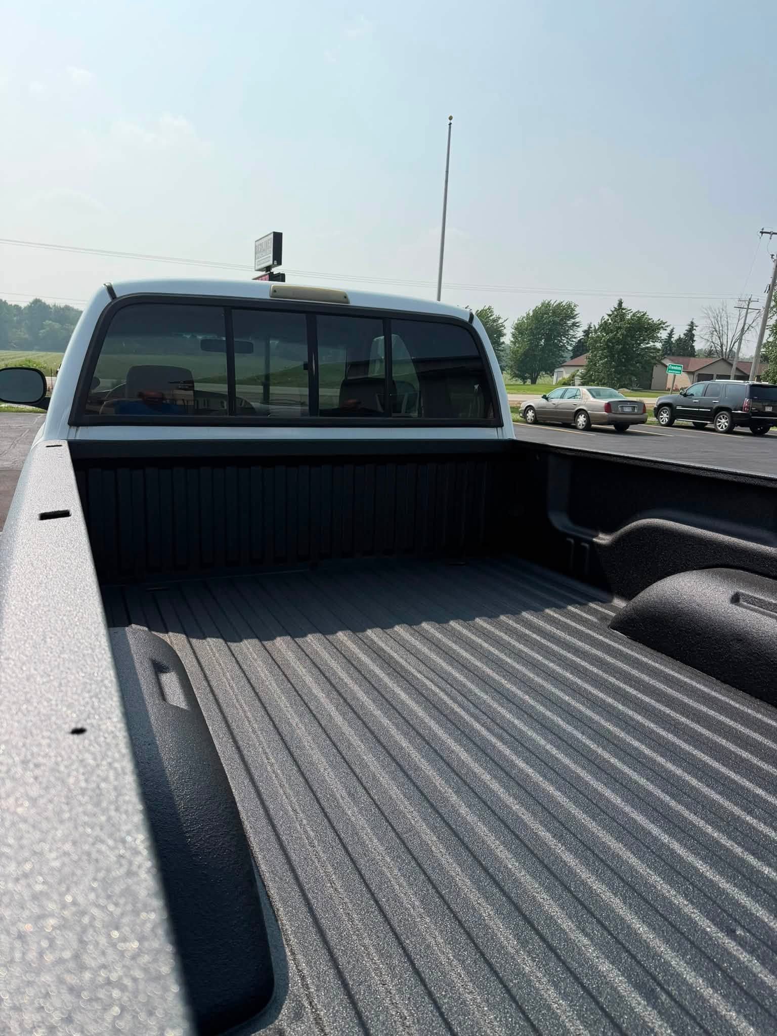 Empty pickup truck bed with ribbed liner, parked outdoors on a sunny day.
