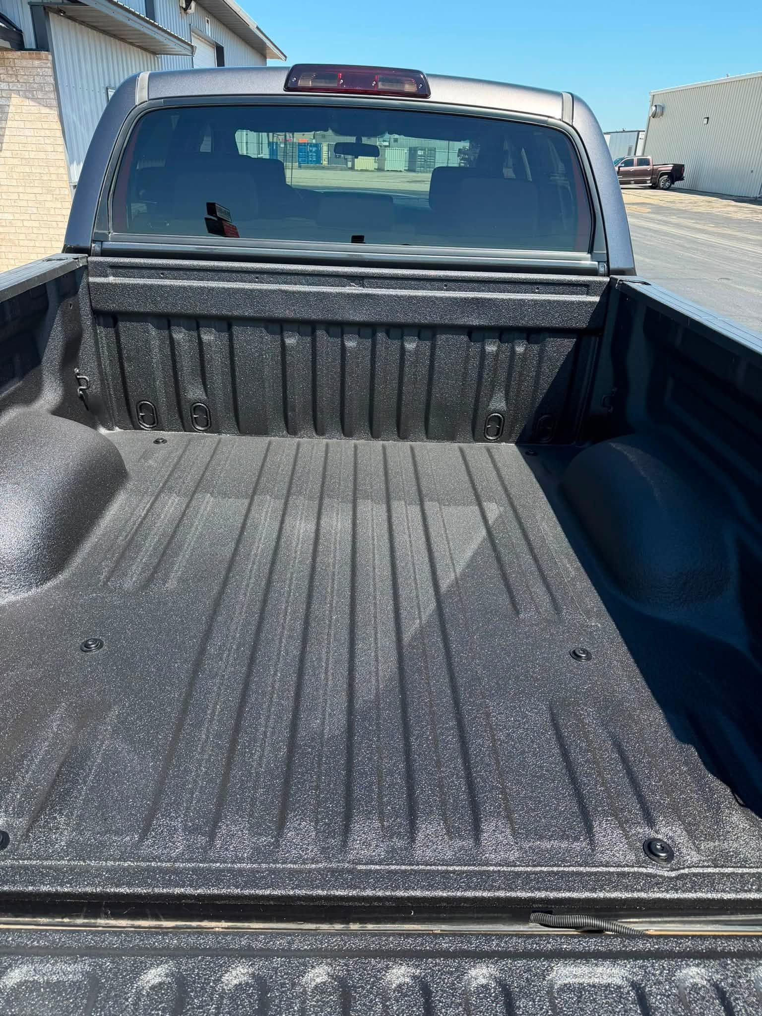 Empty black pickup truck bed with a dusty liner, viewed from the tailgate.
