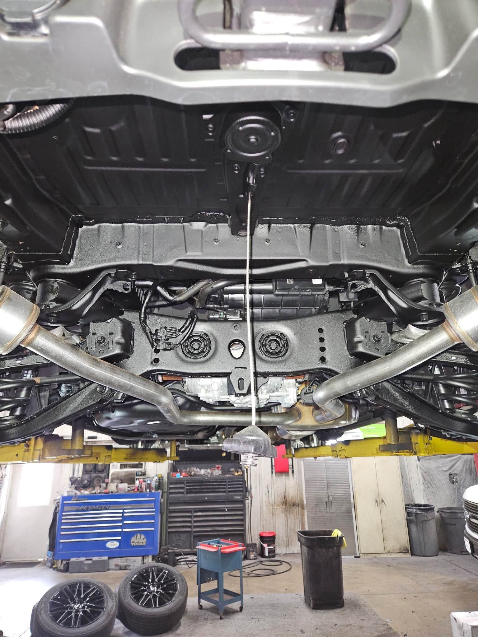 Car undercarriage on a lift in an auto shop, with exhaust and suspension visible.