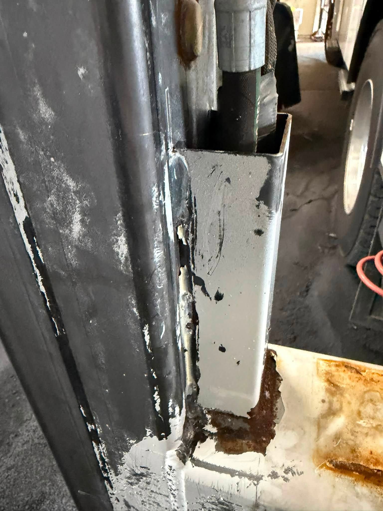Rusty metal hinge on a black door frame with worn white paint and a stained surface.